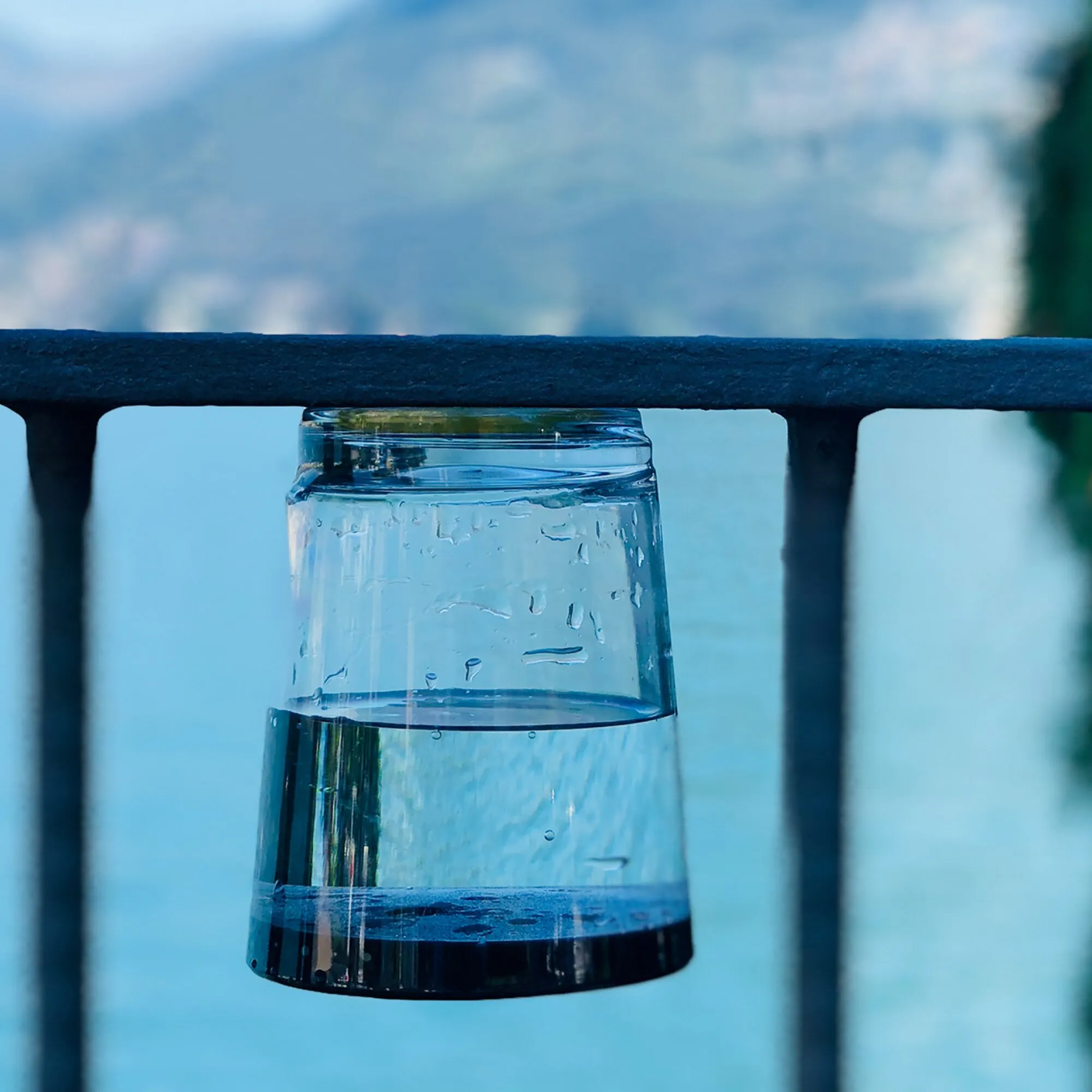 Transparenter Magnet-Trinkbecher mit schwarzem Boden, mit Wasser gefüllt und unter einem dunklen Geländer befestigt, Detailaufnahme