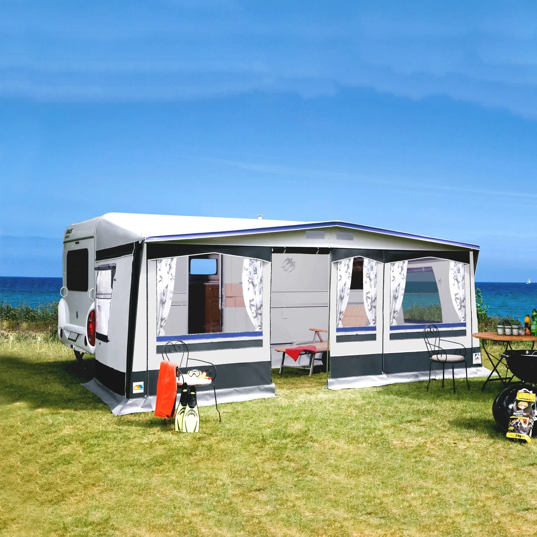 Saisonvorzelt Prestige, 1005 cm, weiß-grau, an einem Wohnwagen mit Fenstern und Vorhängen auf einer Wiese am Meer