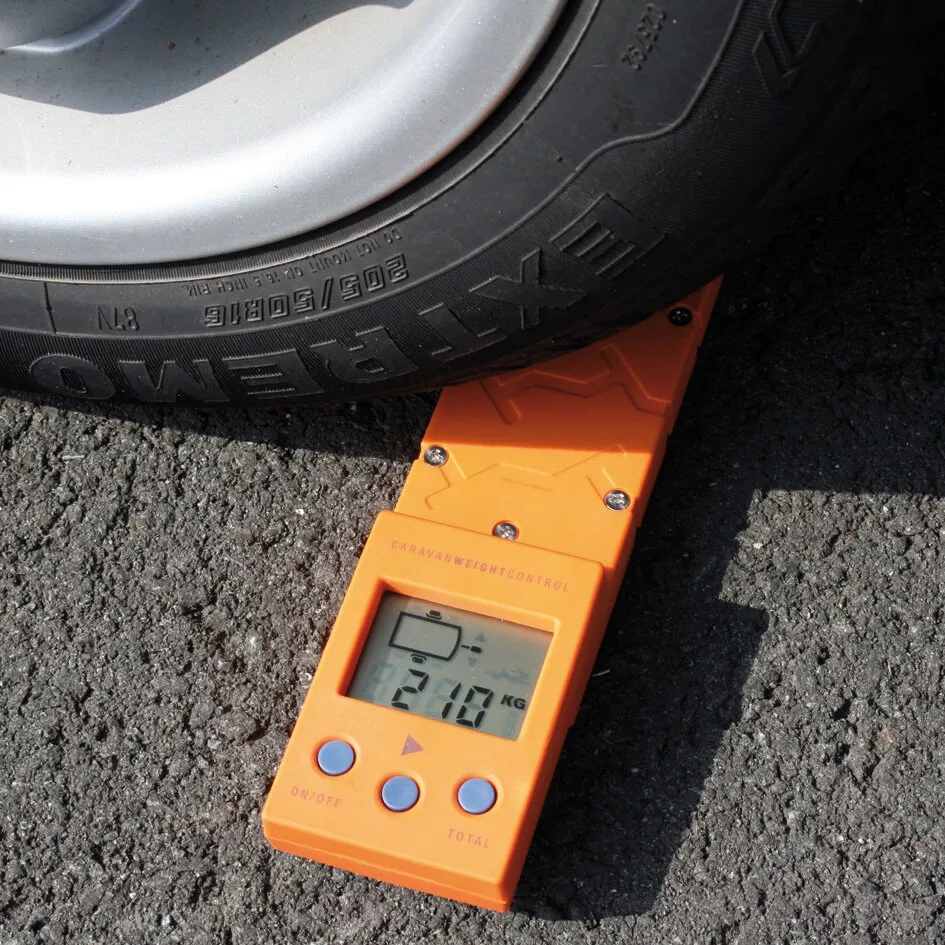 Orangefarbene Stützlastwaage Caravan Weight Control CWC unter einem Autoreifen, Display mit Messwert 270 kg