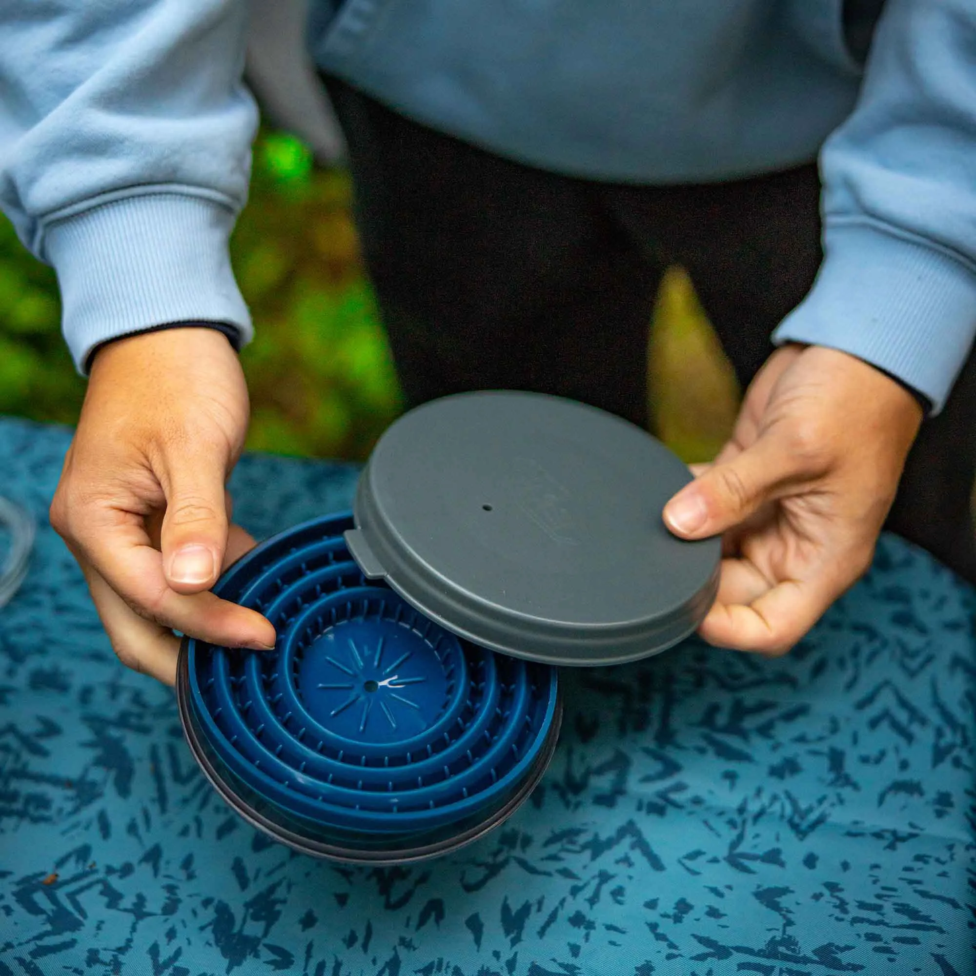 Person setzt einen blauen faltbaren Kaffeefilter der Größe 4 auf einen grauen Deckel auf DIY