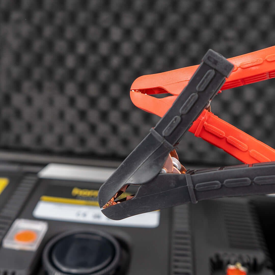 Detailaufnahme einer orangefarbenen und schwarzen Klemme mit freiliegenden Kupferkontakten, vor dem Gehäuse einer Kompressor-Box; Hintergrund unscharfes Display