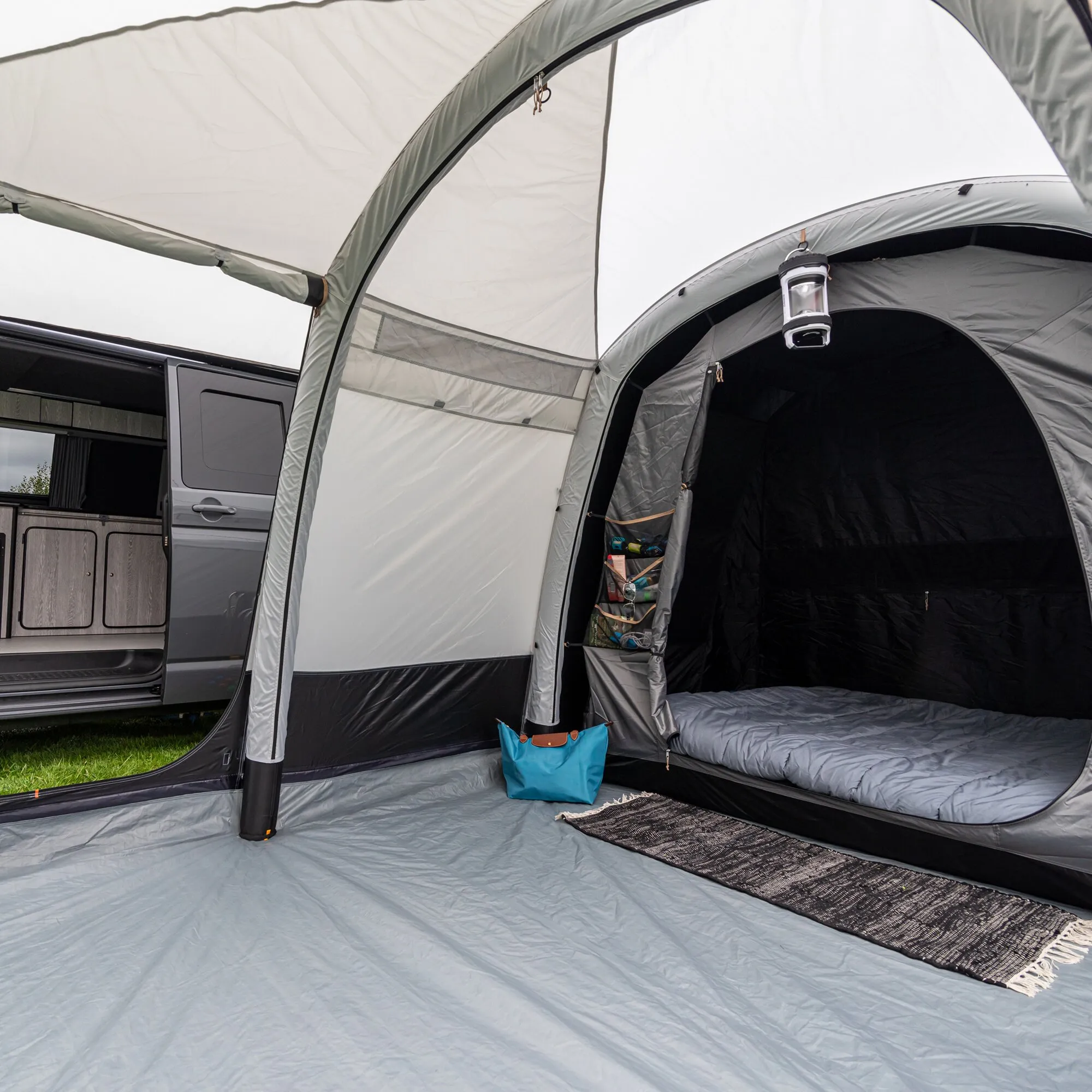 Innenansicht des grauen Busvorzelts Journeymaster Deluxe L mit abgetrenntem Schlafbereich, Bett, LED-Lampe und Ablagefächern am Campingbus