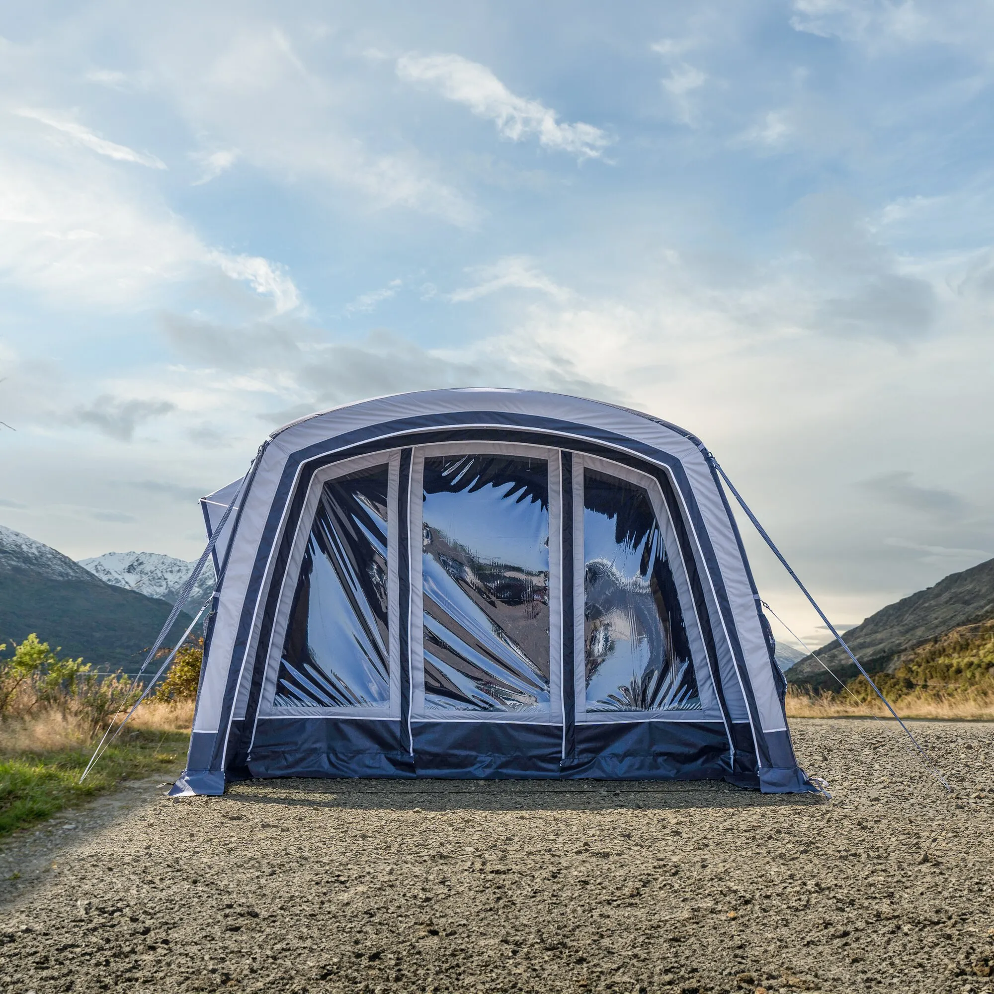 Blau-weißes Busvorzelt Aquila Pro mit transparenten Frontfenstern, abgespannt vor Berglandschaft auf steinigem Untergrund