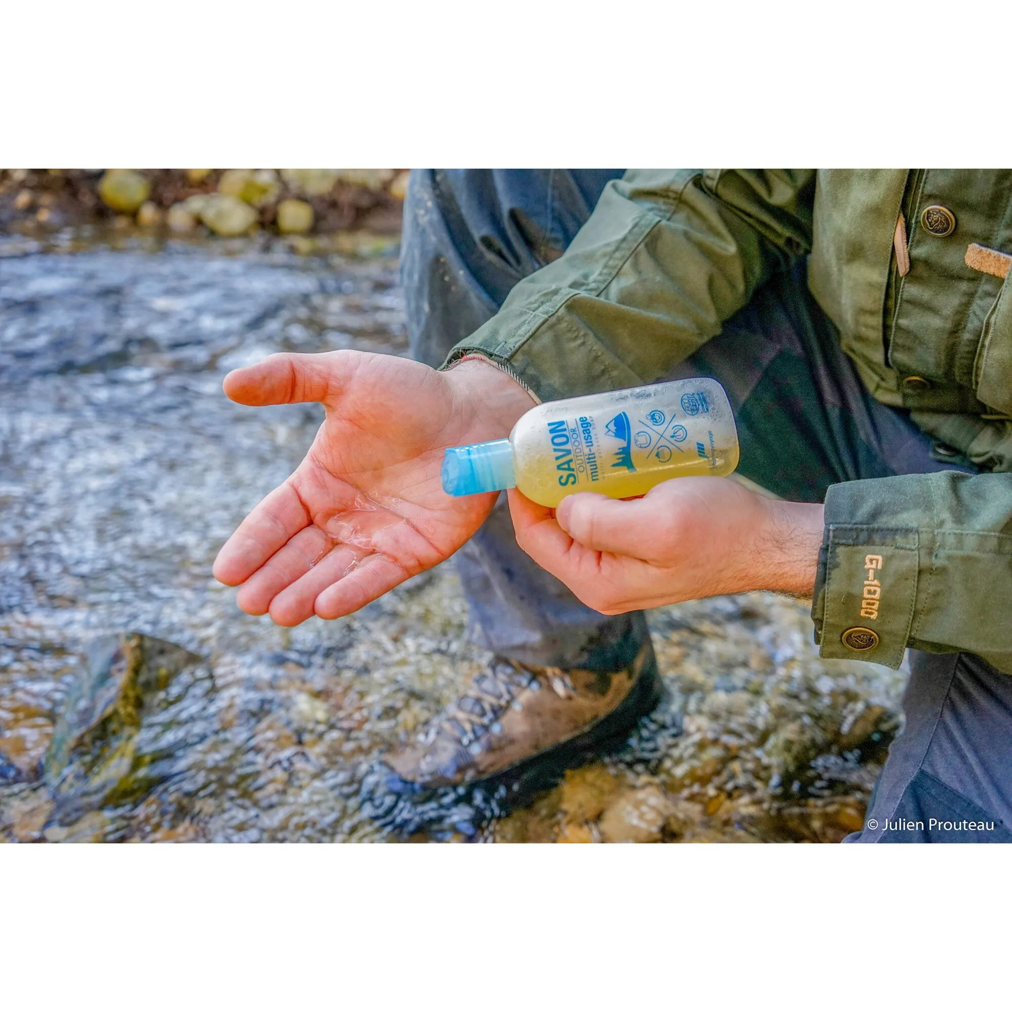 Person wäscht sich am Bach die Hände mit der gelben SAVON OUTDOOR multi-usage Flüssigseife in einer transparenten Flasche