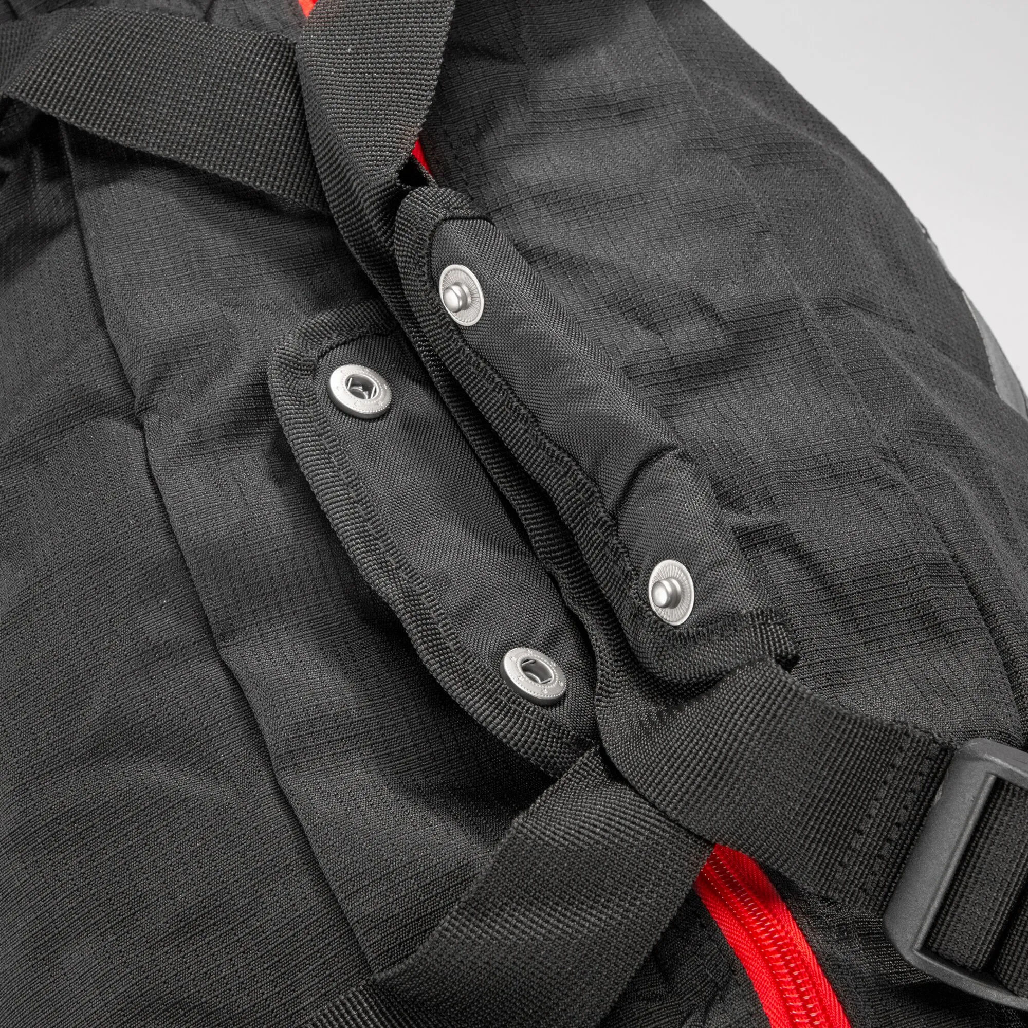Detailaufnahme der schwarzen Reisetasche Cosmos Duffle 50S mit gewebtem Material, Tragegurten, Druckknöpfen, Schnalle und roten Akzenten