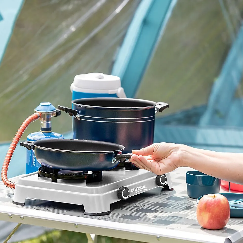 Campingaz Camping Cook CV Campingkocher mit zwei schwarzen Kochplatten, Topf und Pfanne im Zeltbetrieb, Hand am Pfannengriff