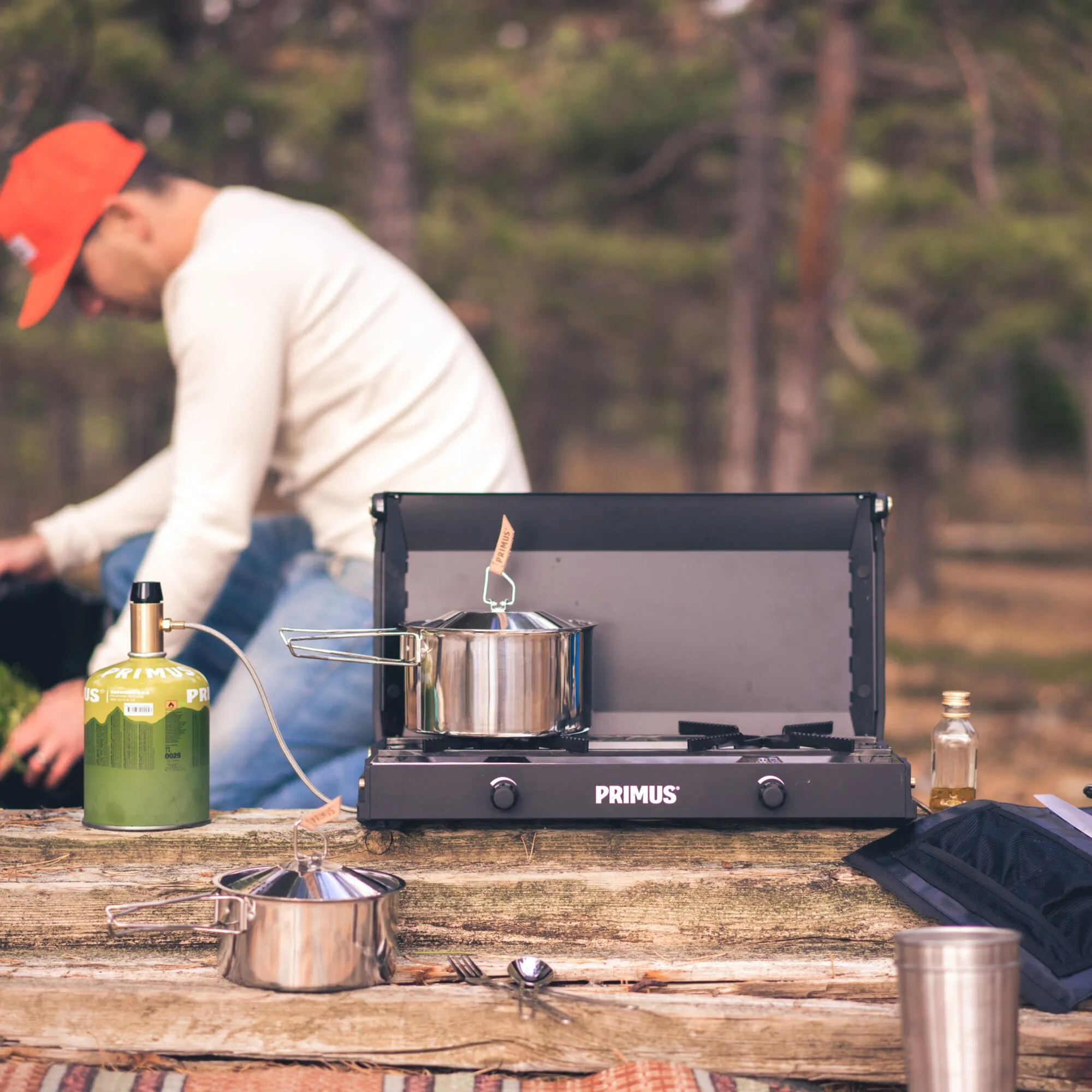 Schwarzer Primus Kinjia Stove mit zwei Kochstellen, Topf und Gasflasche auf einem Holztisch im Wald