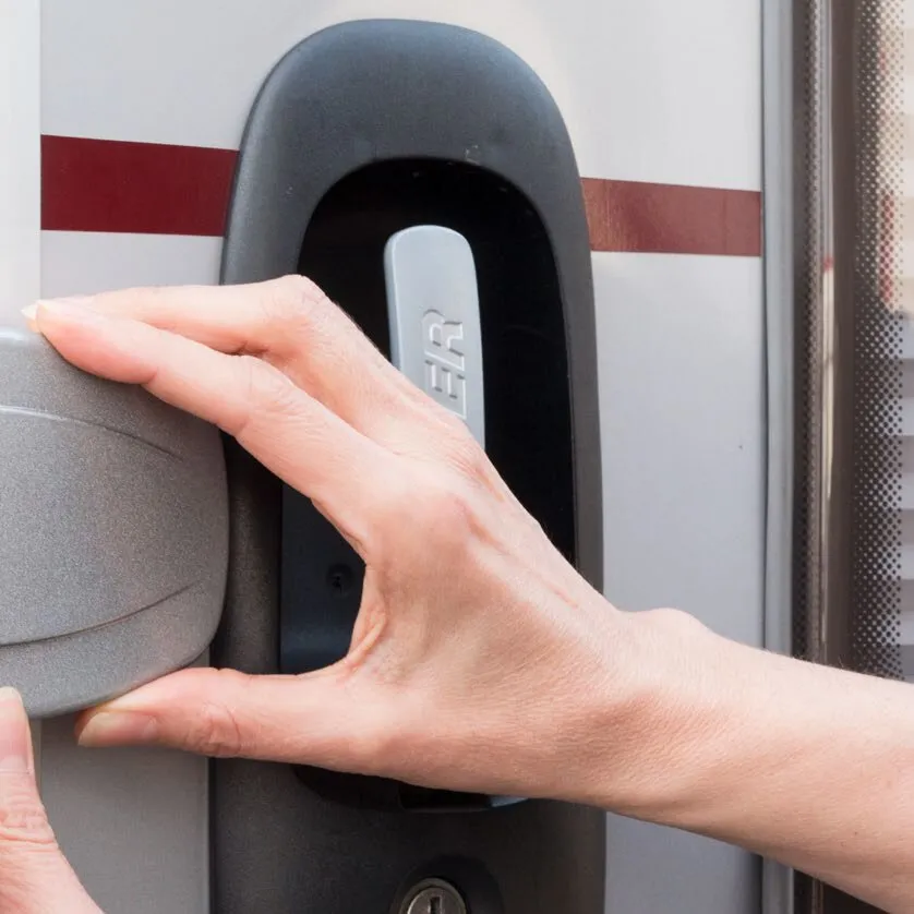 Hand einer Person bedient die schwarze Türsicherung Safe Door an einer grauen Fahrzeugtür; zentraler silberner Hebel sichtbar