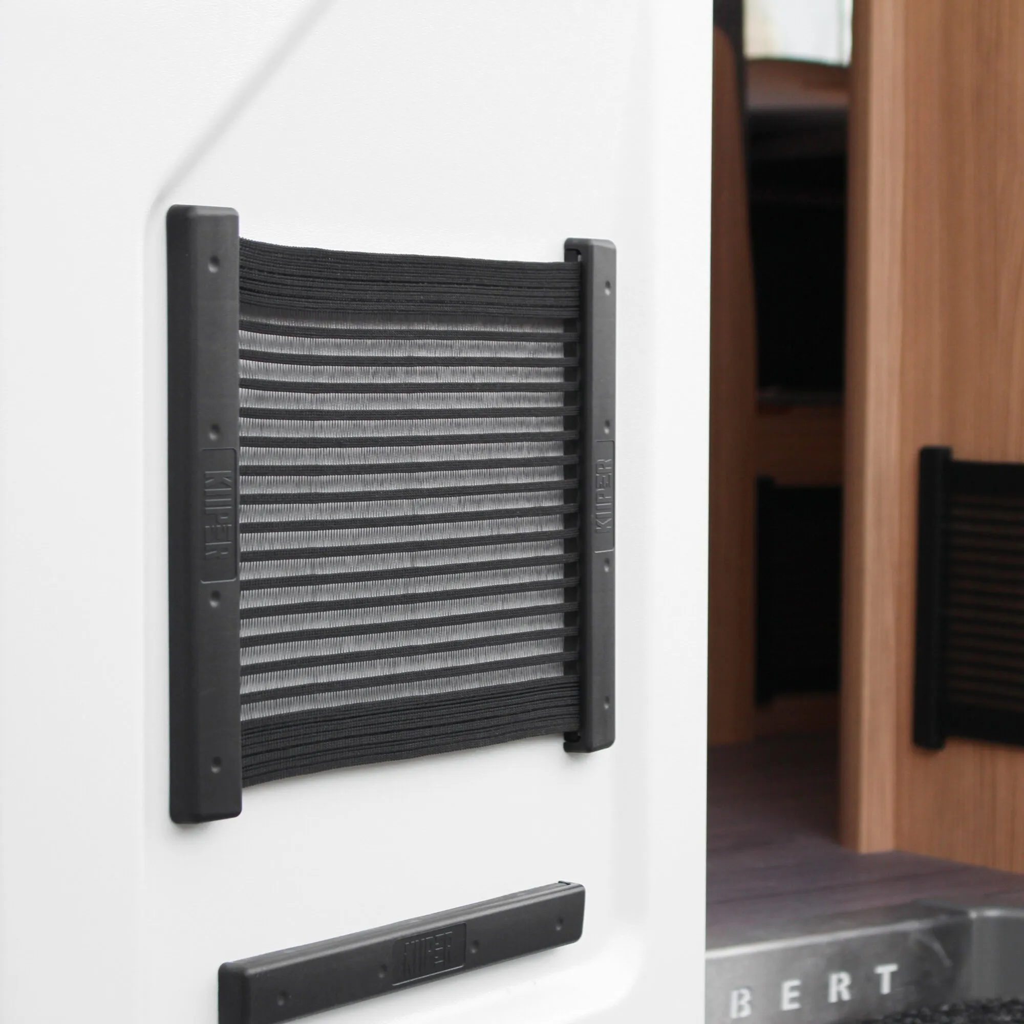 Schwarzes Ablagenetz KiiPER L mit elastischen Querfächern, an einer weißen Wand neben einem Holzschrank montiert