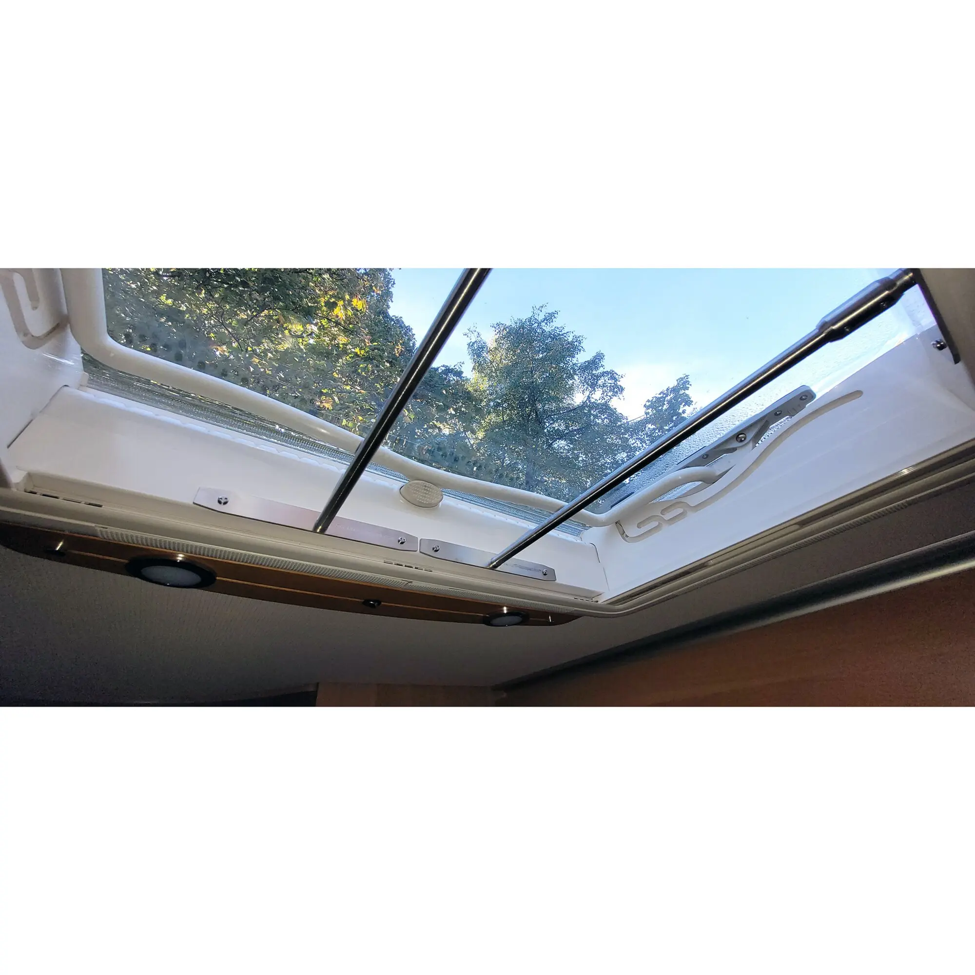 Innenansicht eines Wohnmobils mit Dachhaubenschutz Midi Heki Style 2, weißem Rahmen und großem Panorama-Dachfenster, Blick auf Himmel und Baumkronen