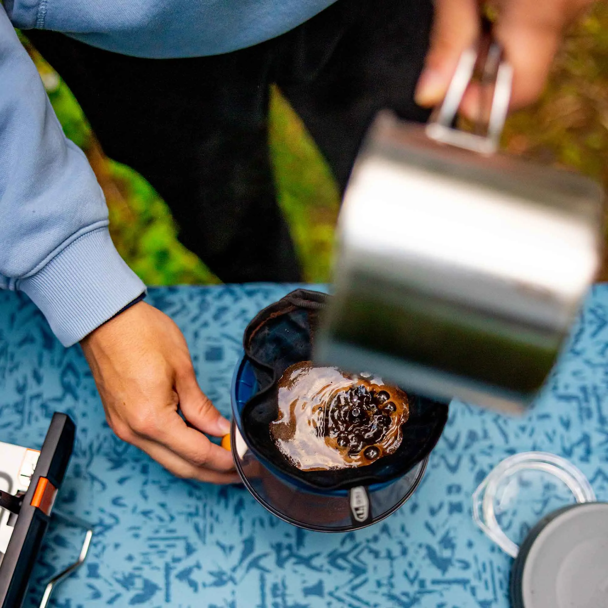 Person brüht Kaffee mit einem schwarzen wiederverwendbaren Kaffeefilter über einer Glaskanne auf einem Tisch bevertalt Teppich