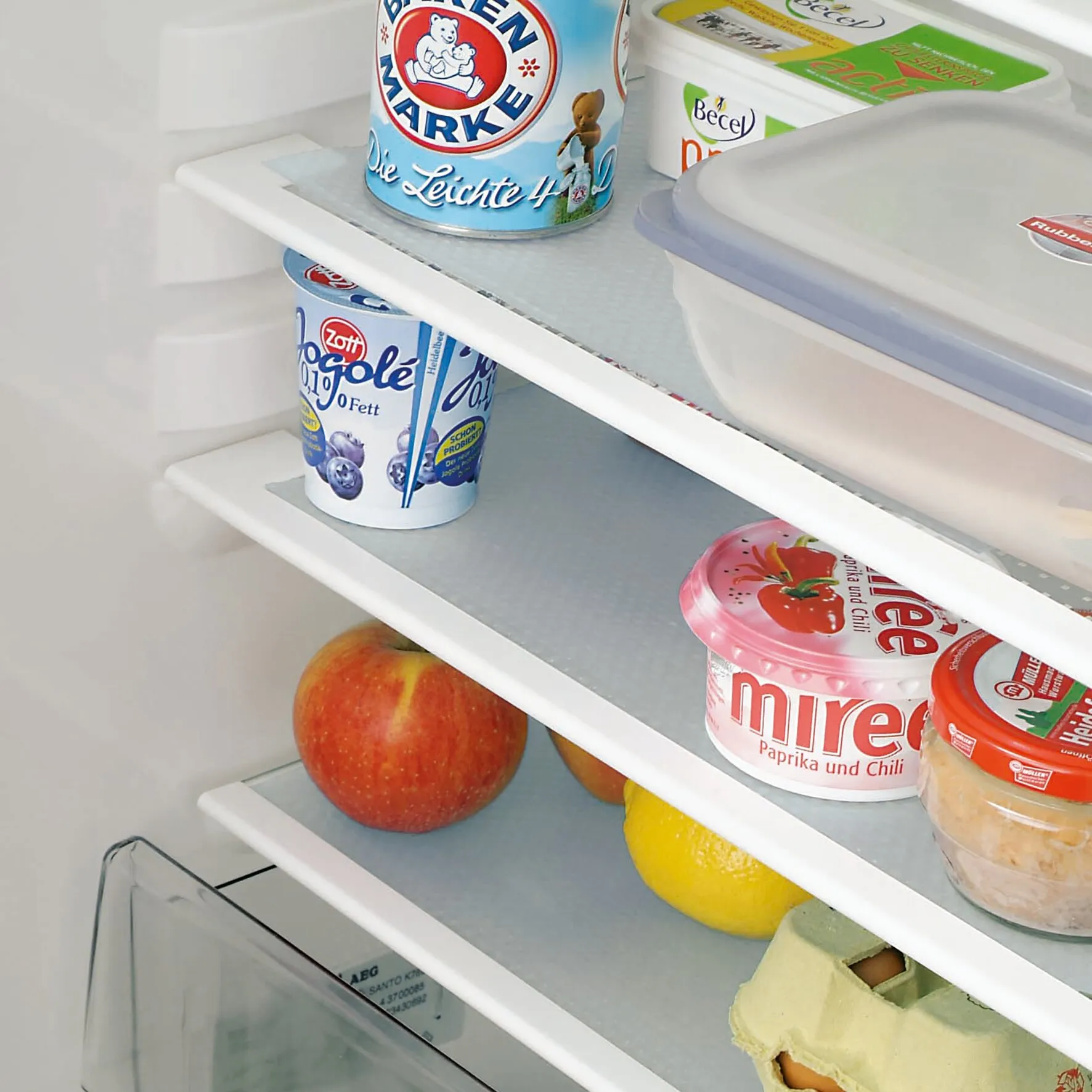 Graue Antirutschfolie Cool & Fresh liegt auf mehreren Kühlschrankablagen und hält Lebensmittelbehälter sowie Obst rutschfest an ihrem Platz