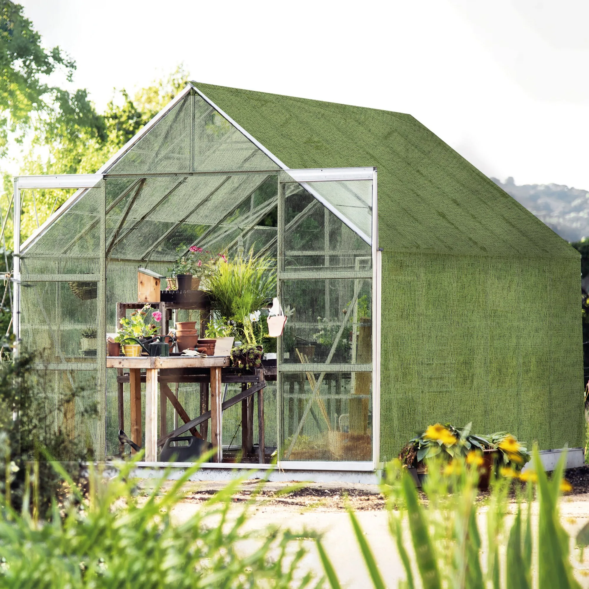 Grüner Aero-Tex-Vorzeltteppich mit feinmaschiger Struktur an einem Gewächshaus mit Topfpflanzen im Garten