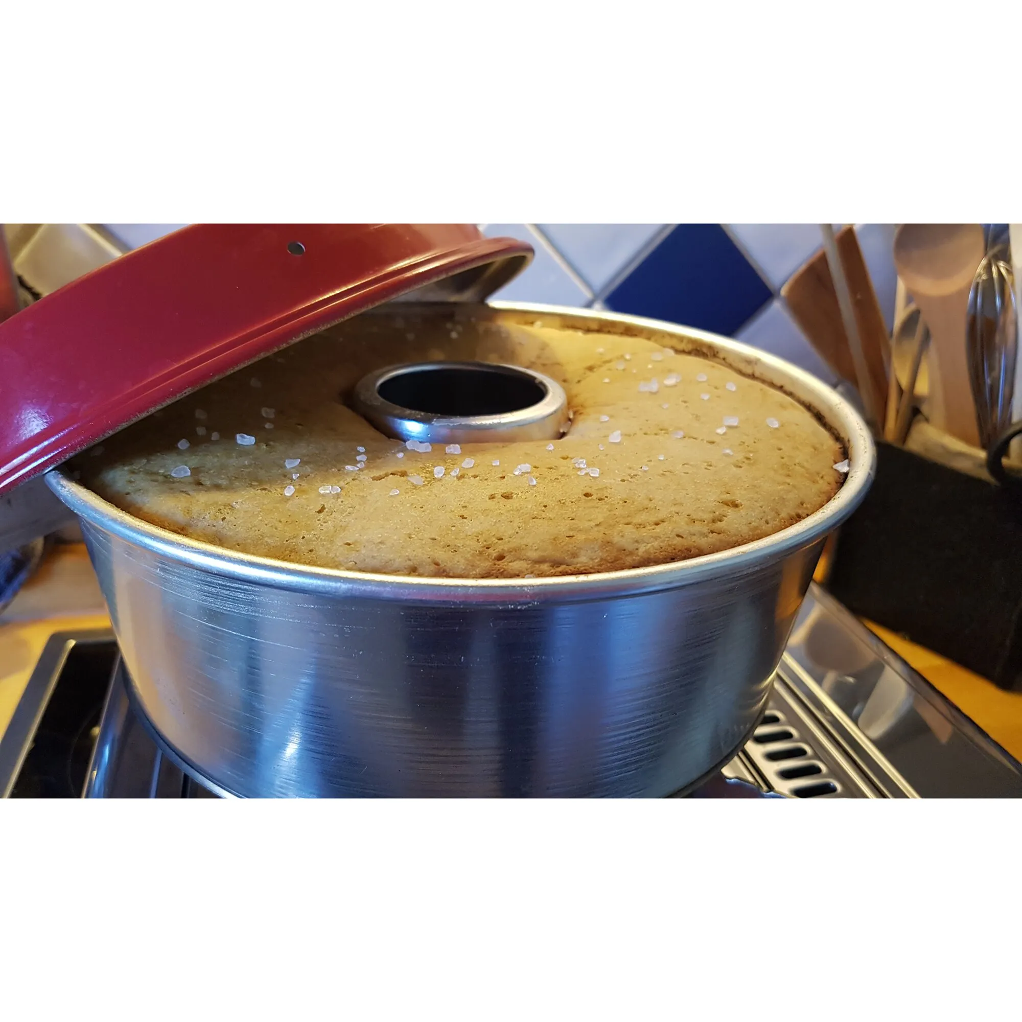 Metallene Backform Maxiform 3L mit zentralem Rohr, gefüllt mit gebackenem Kuchen und grobem Salz, auf einem Herd mit rotem Deckelાજુ