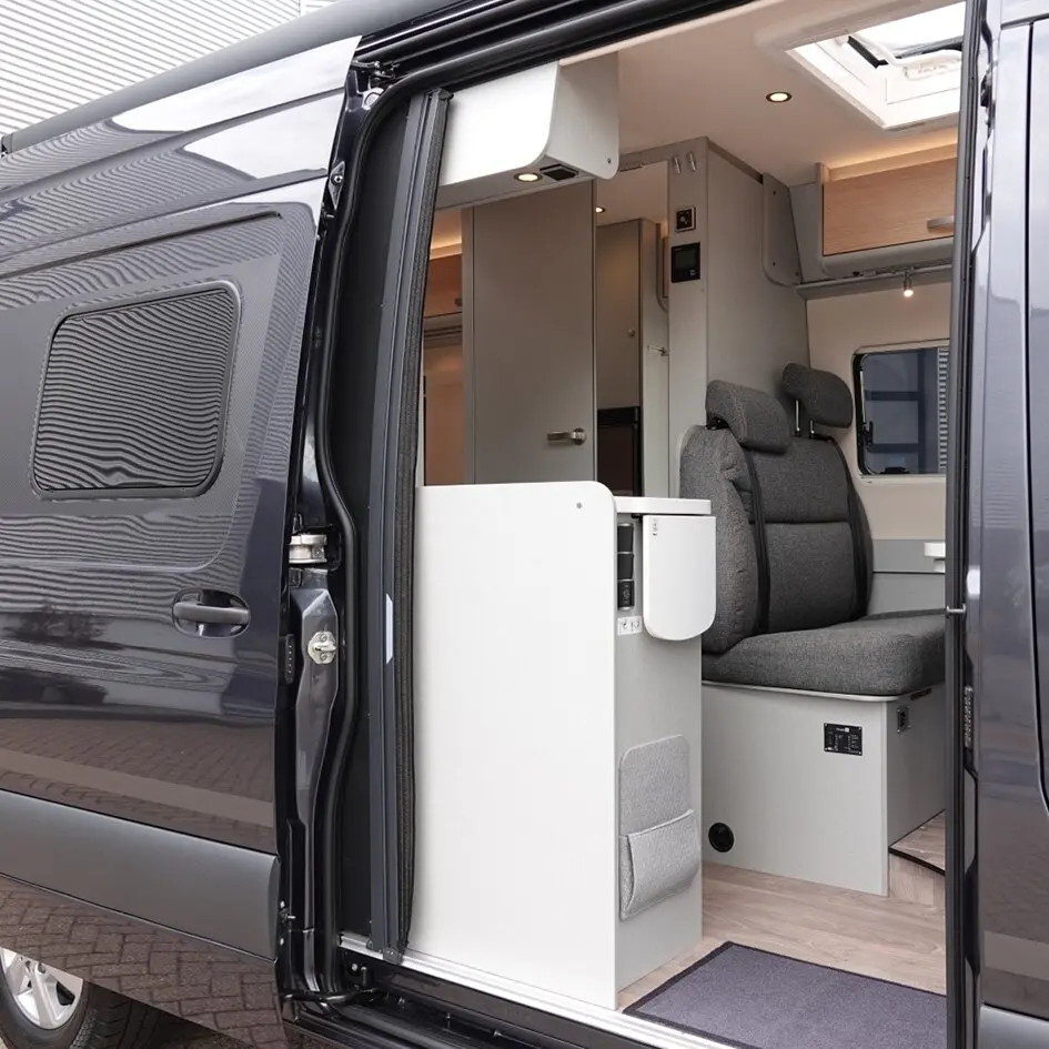 Offene Seitentür eines Camper-Vans mit grauer Innenausstattung, zwei Sitze, Holzboden und Plissee-Fliegenschutz-Tür im Türbereich