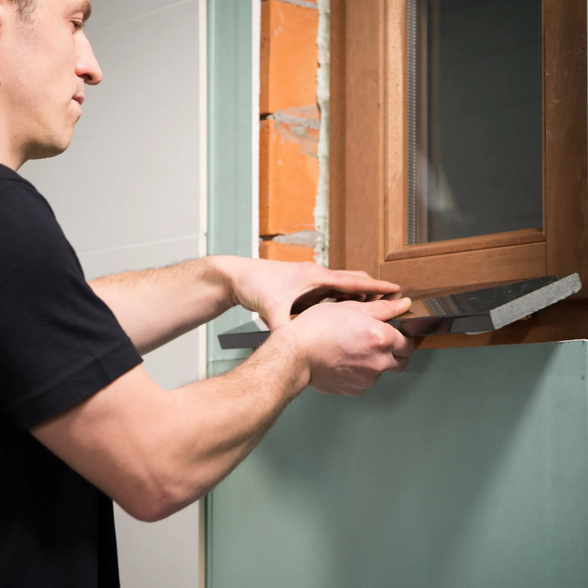 Handwerker richtet einen schwarzen Dichtungsstreifen am unteren Rahmen eines Holzfensters aus