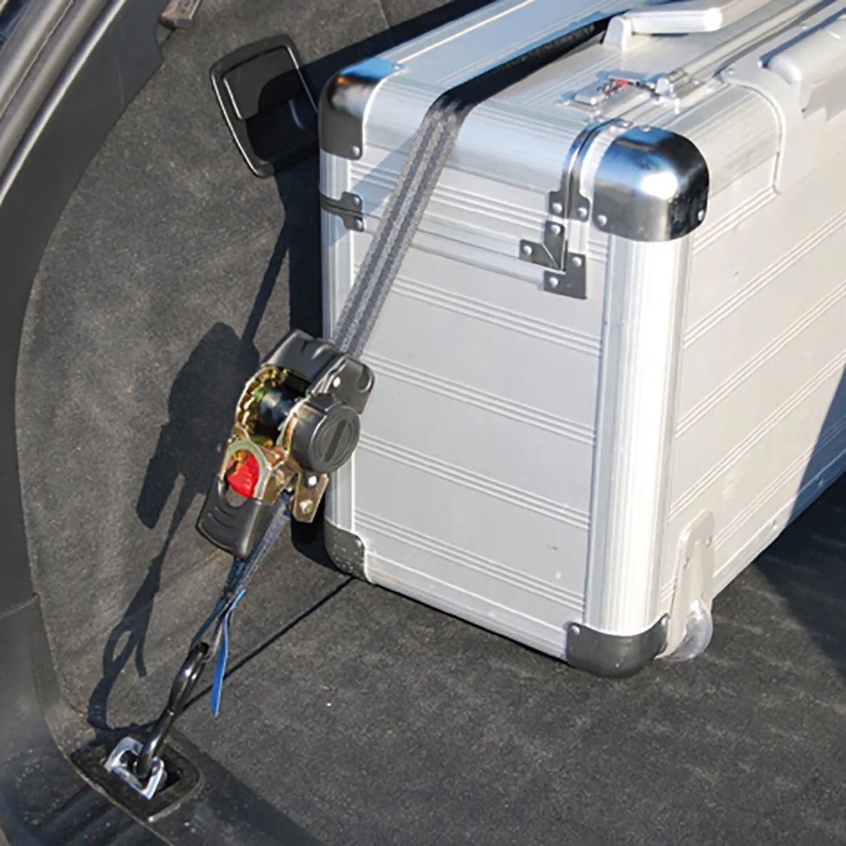 Auto Cargo Belt sichert einen silbernen Aluminiumkoffer im Kofferraum mit Ratsche und Haken an Verzurrösen