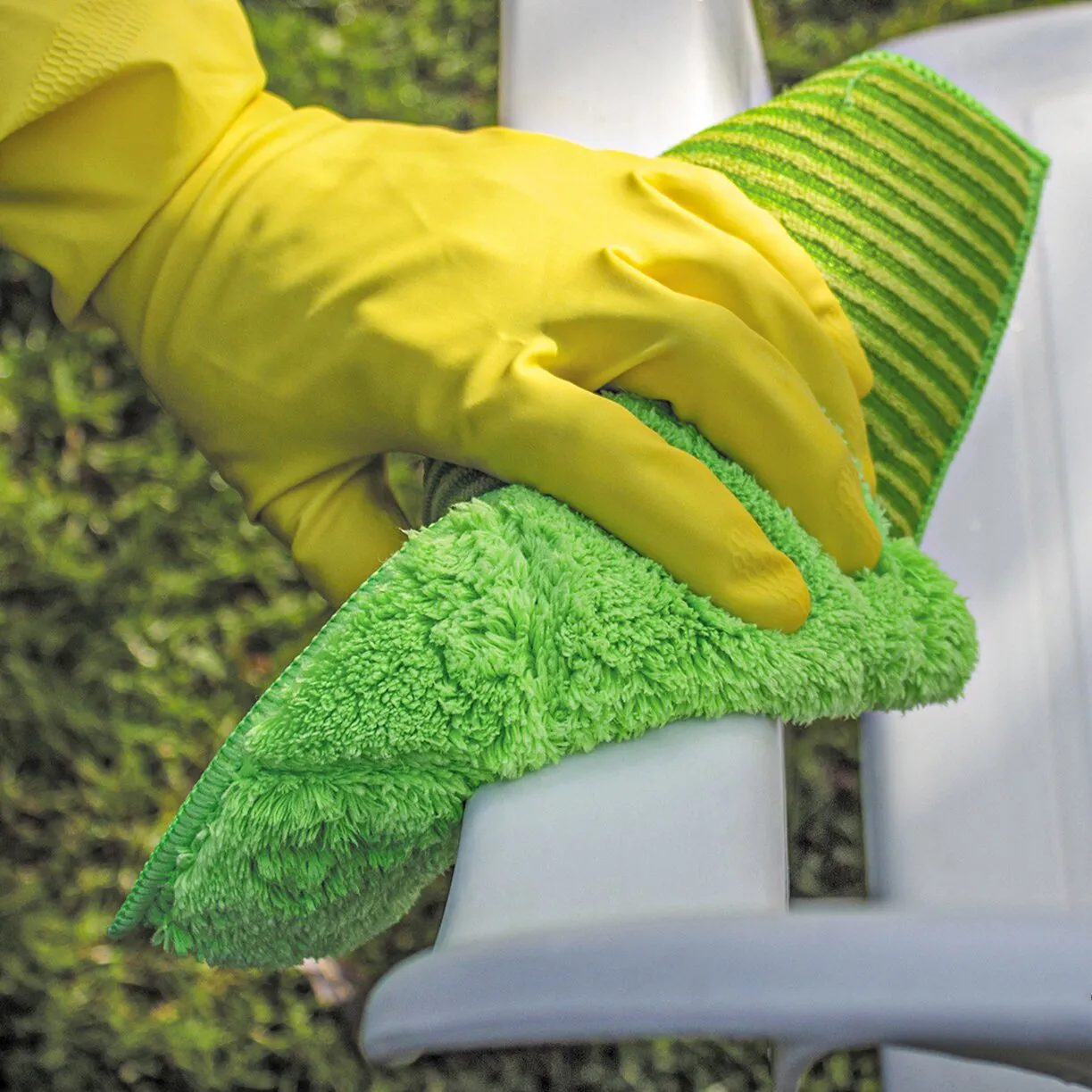 Grünes Bambustuch wird von einer Hand mit gelbem Reinigungshandschuh an einem weißen Geländer verwendet