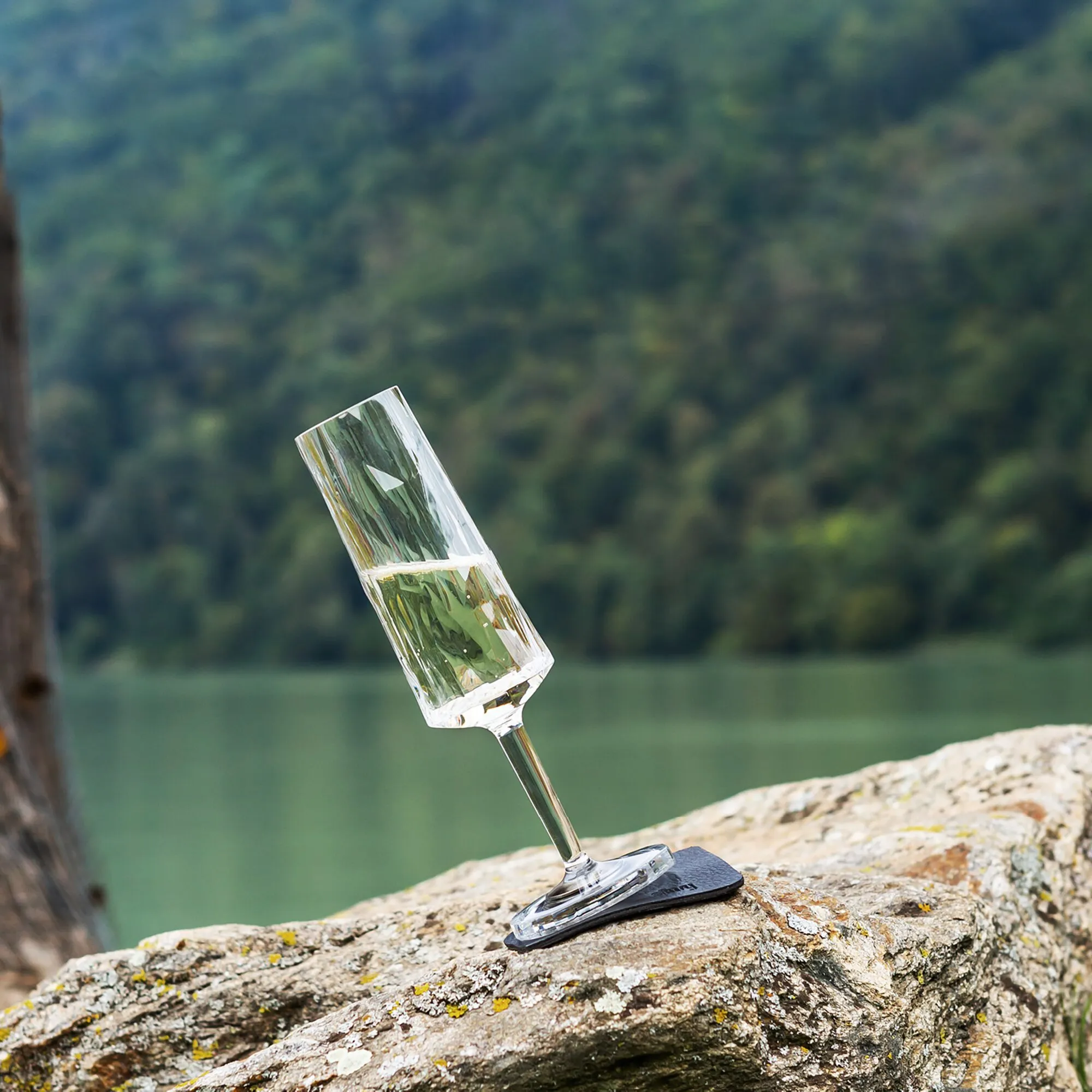 Transparentes Magnet-Kunststoffsektglas mit grünlichem Getränk steht schräg auf einem schwarzen Magnetfuß auf einem Felsen
