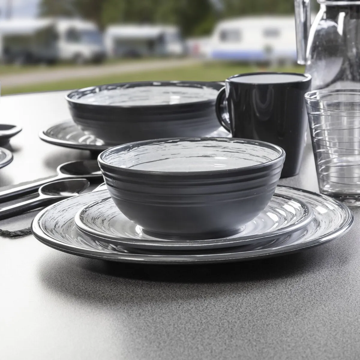 Geschirrserie Granada in Schwarz und Grau mit Schalen, Tellern, Tasse, Gläsern und Karaffe auf einem Tisch im Freien