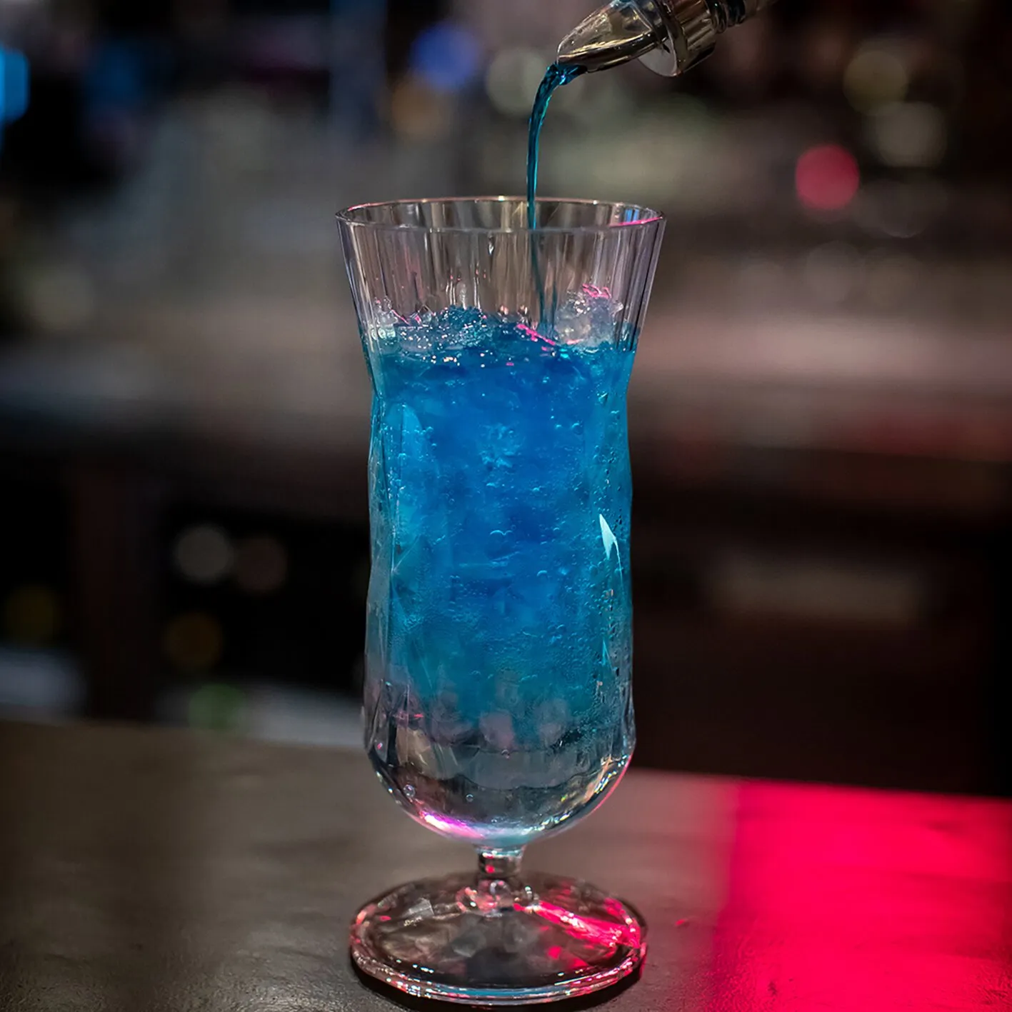 Klares Superglas CLUB Cocktailglas mit blauem Getränk und Eis, während es aus einer Flasche eingeschenkt wird