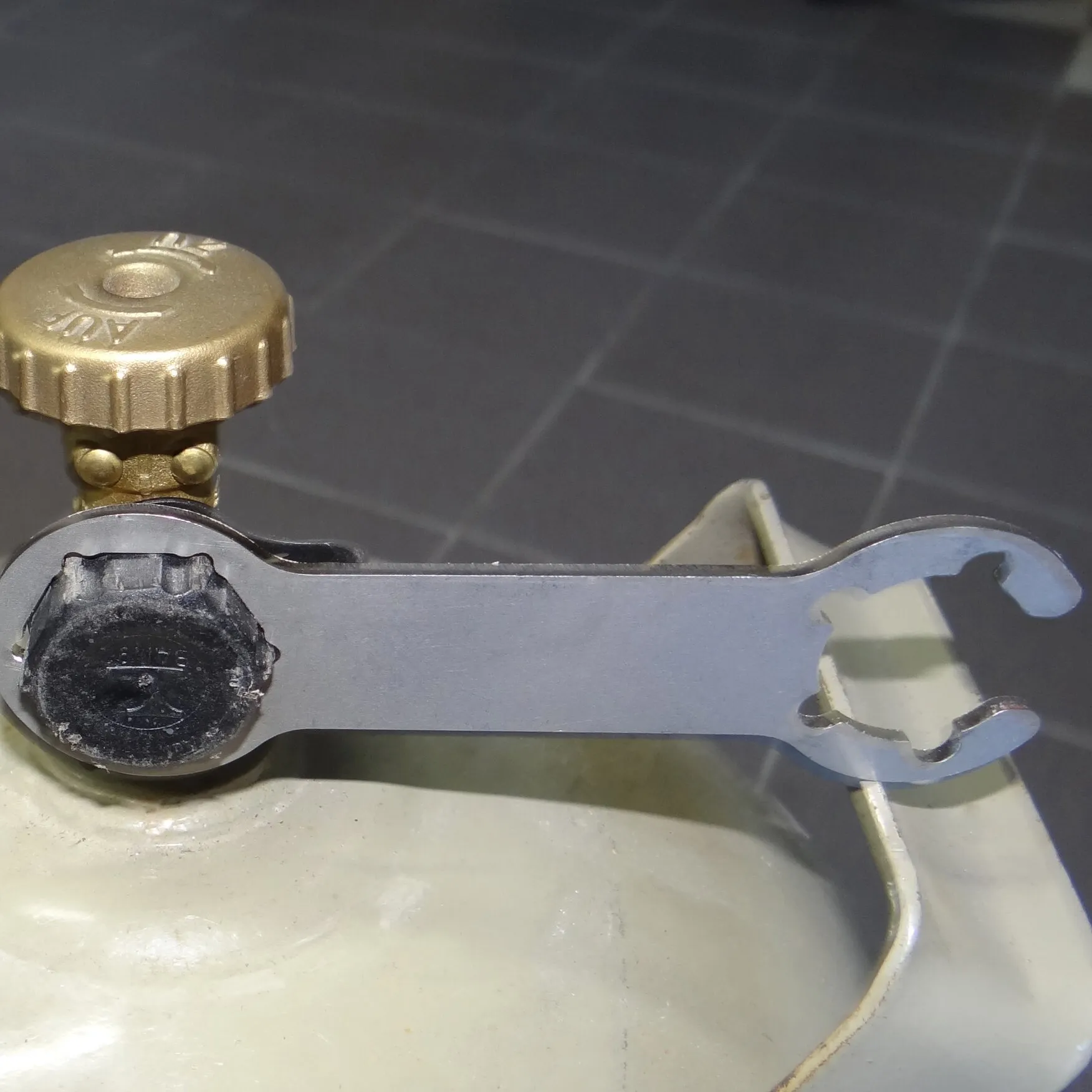 Silberner Gasflaschenschlüssel aus Metall sitzt an einem schwarzen Gasregler mit goldener Überwurfmutter auf einer Gasflasche