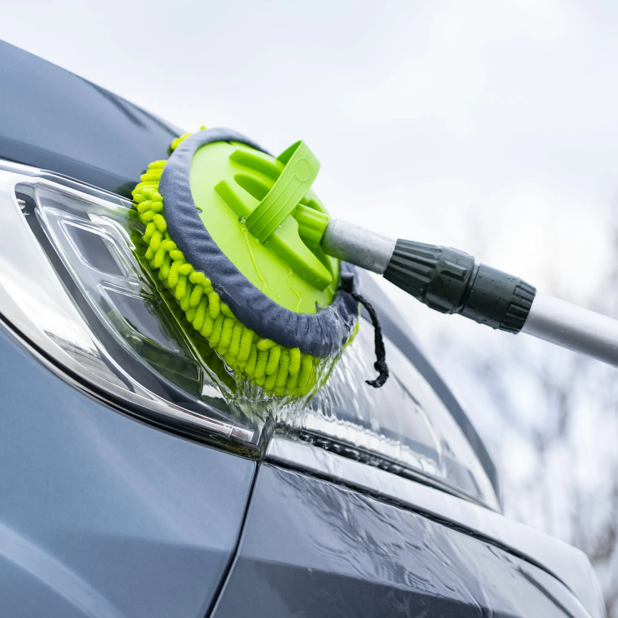 Grüner Mopp-Aufsatz mit Mikrofaserbezug beim Reinigen der nassen Windschutzscheibe eines Autos