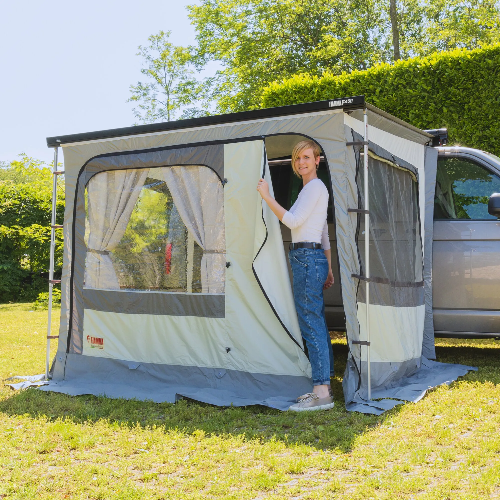Graues Markisenzelt Privacy Ultra Light von Fiamma an einem Wohnmobil, mit transparenten Fenstern und einer Frau beim Öffnen der Tür