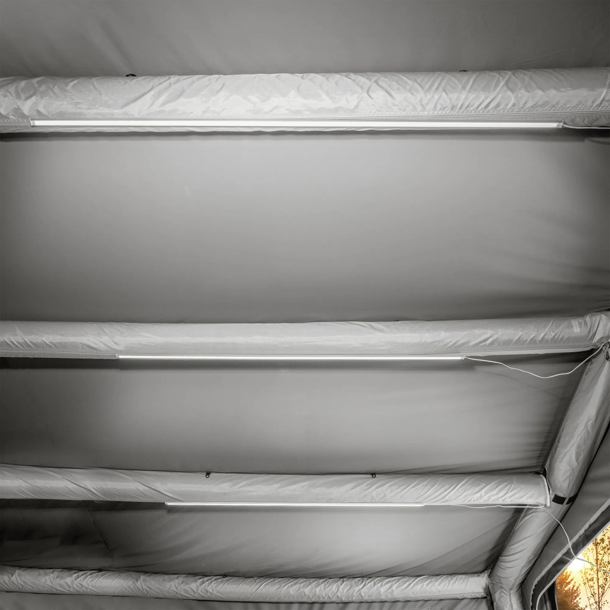 Drei weiße LED-Lichtleisten sind an den Stoffstreben eines Vorzelts montiert und beleuchten dessen Innenraum