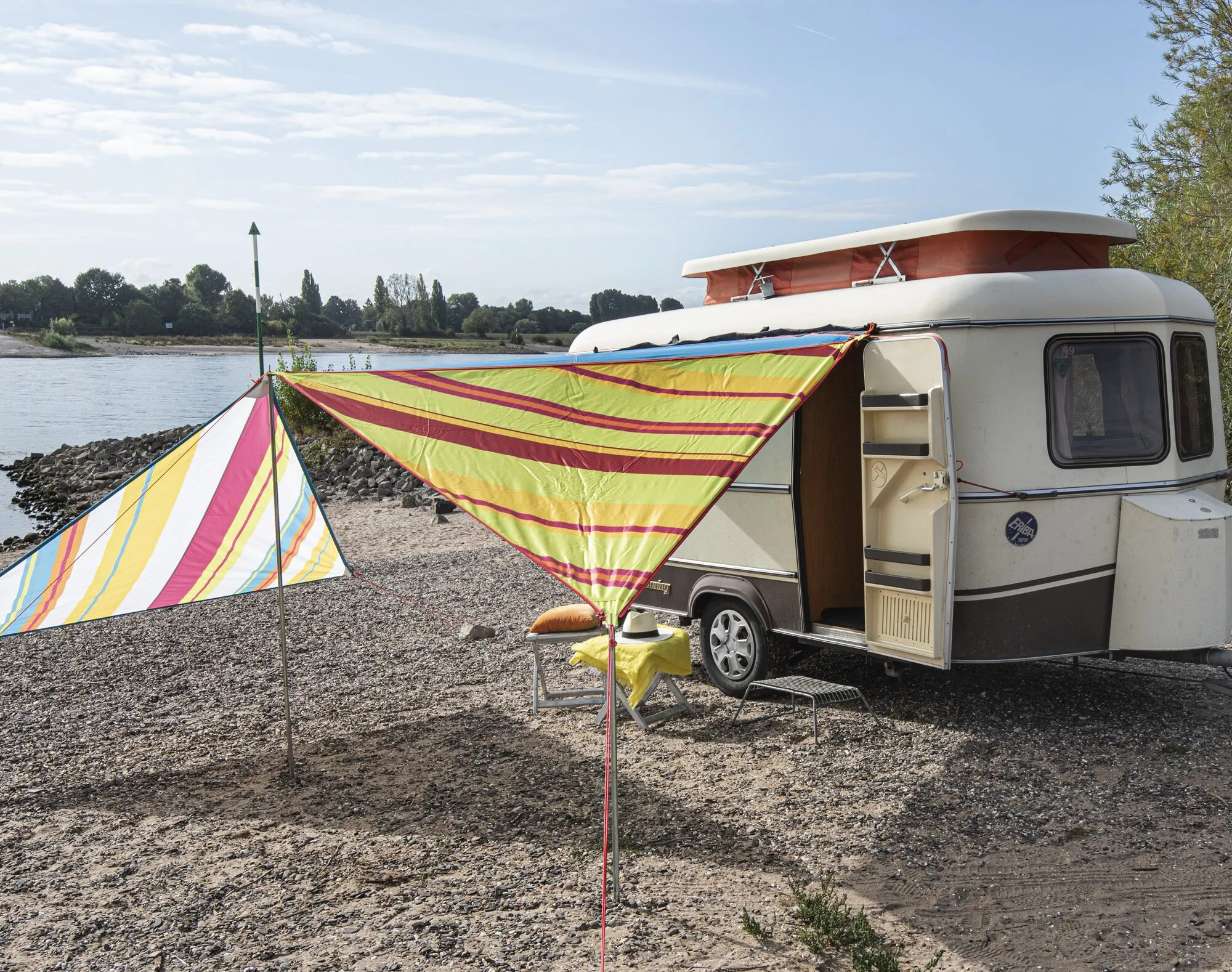 Limefarbenes, gestreiftes Sonnensegel Zip Canvas Caribbean am Wohnwagen auf einem kiesigen Uferplatz aufgebaut