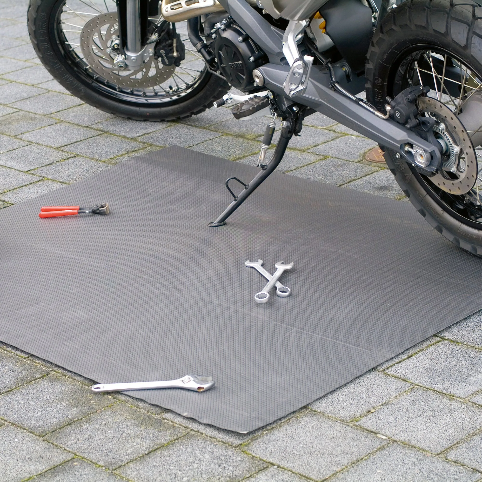 Graue Kofferraum- und Schmutzfangmatte mit rutschhemmender Struktur unter einem Motorrad mit darauf liegenden Werkzeugen