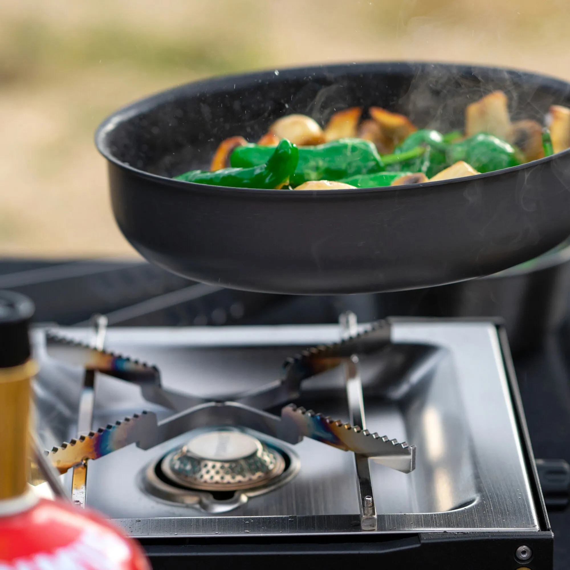 Schwarze Pfanne mit grünem und gebratenem Gemüse auf dem silbernen Moja Stove Gaskocher in Nahaufnahme
