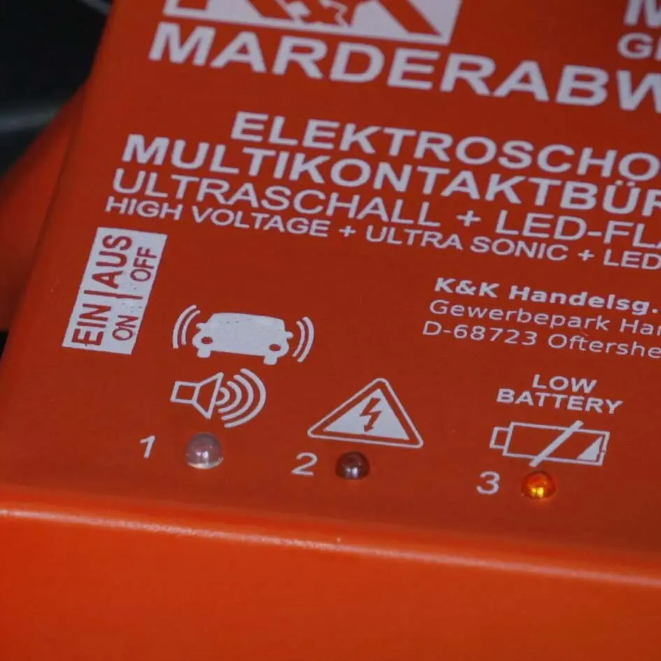 Orangenes Marderabwehrgerät mit Ultraschall und Hochspannung; Ein/Aus-Schalter, Lautsprecher-Icon, Hochspannungssymbol und drei LEDs 1–3