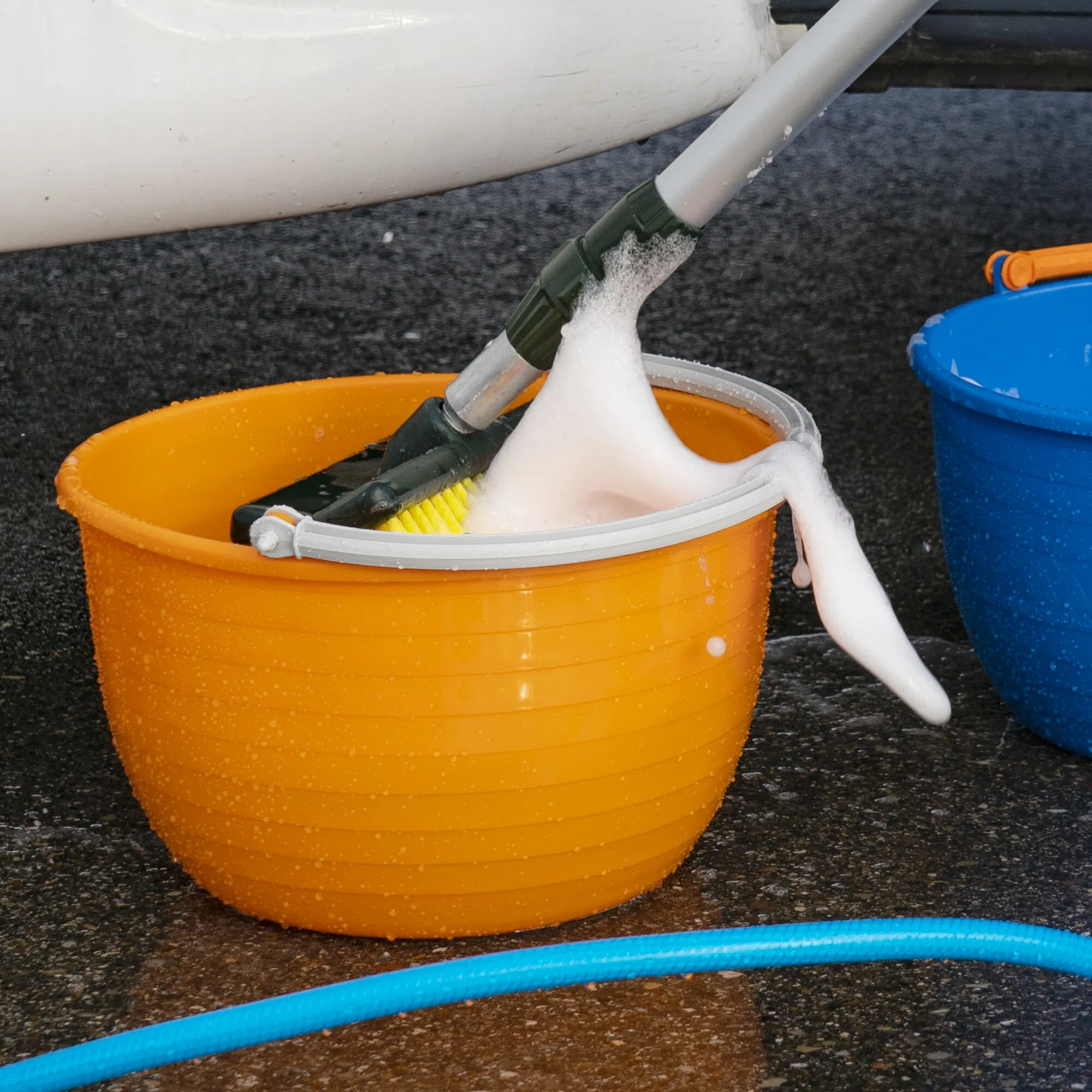Oranger Vielzweckeimer Vinis mit weißem Tragebügel, Bürste und Schaumwasser beim Reinigen eines Pools neben einem blauen Eimer