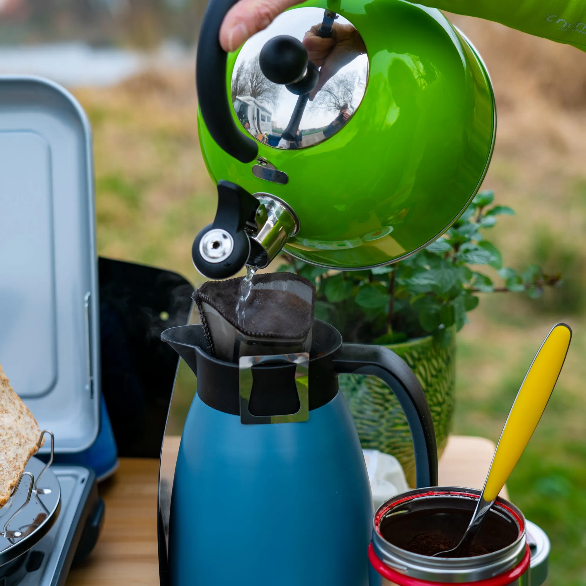 Grüner Flötenkessel Trend Color mit schwarzem Griff gießt Wasser in einen Kaffeefilter im Freien
