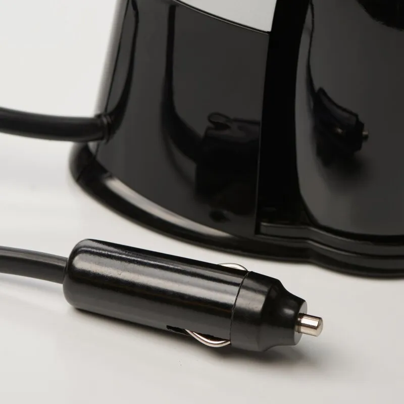 Detailaufnahme einer schwarzen Kaffeemaschine mit angeschlossenem Stromkabel und sichtbarem 12-Volt-Stecker auf hellem Untergrund