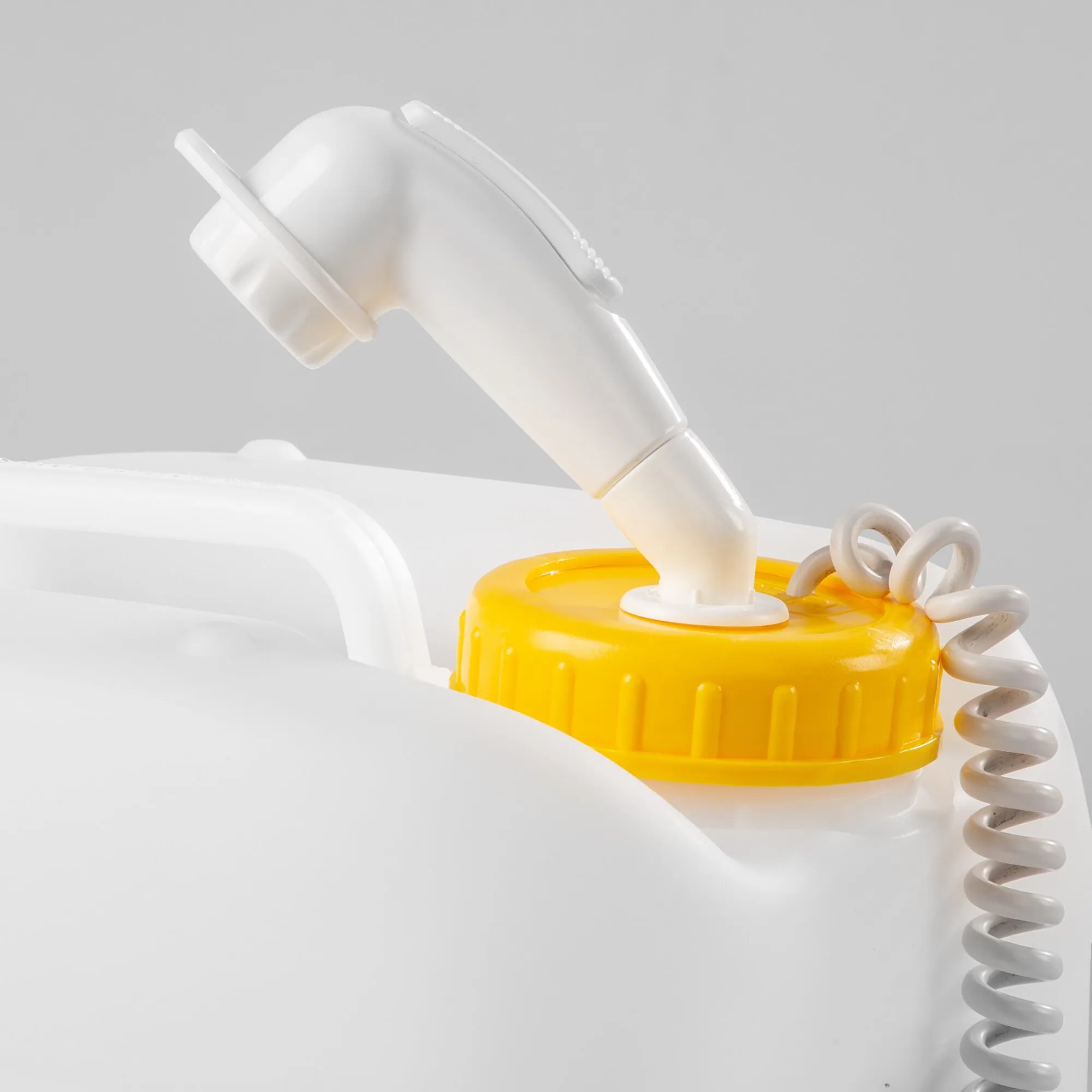 Weiße Handbrause einer Kfz-Mobildusche mit Spiralschlauch und gelbem Anschlussgehäuse in Detailaufnahme