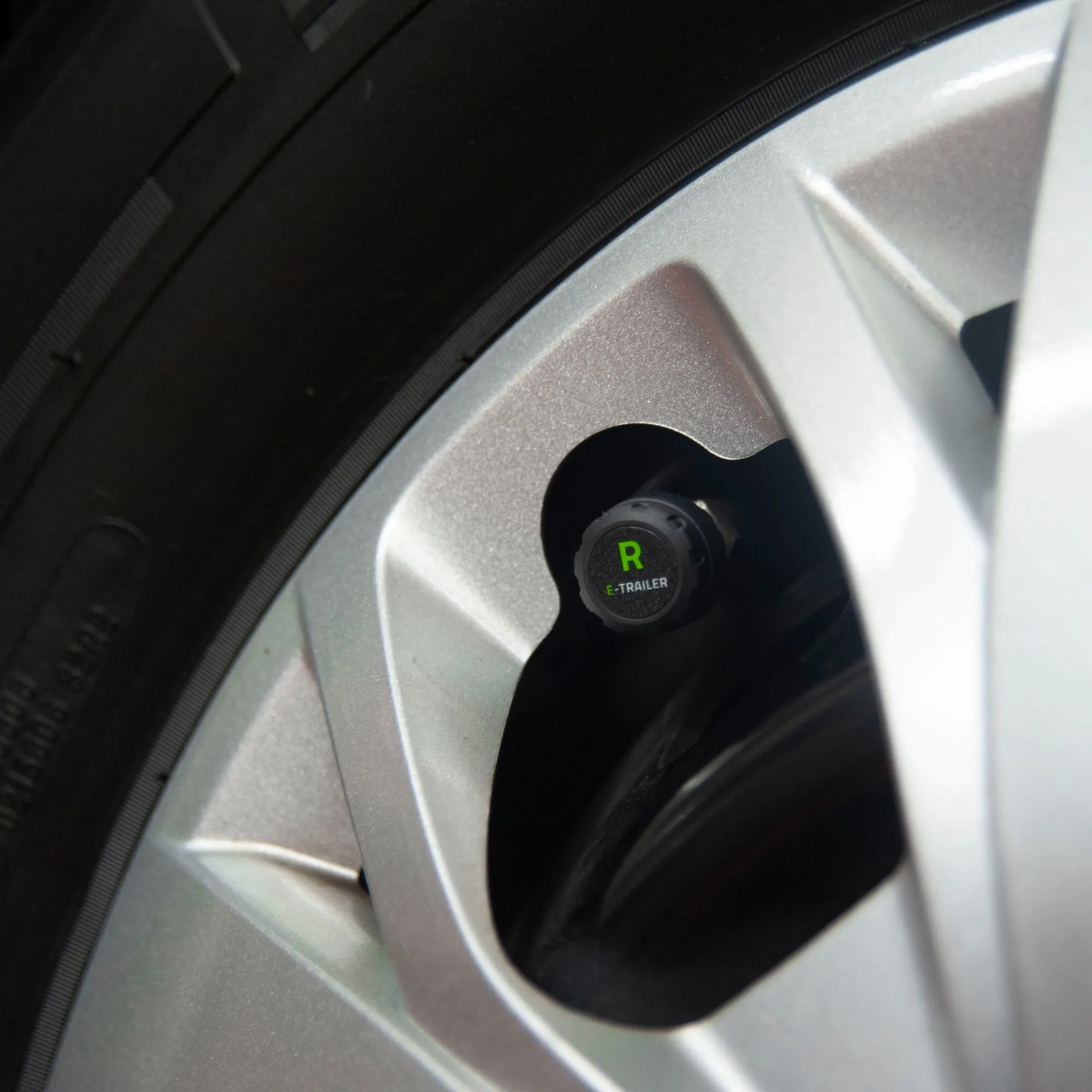 Nahaufnahme eines schwarzen E-Pressure-Sensors mit grüner R-Markierung am Ventil eines Reifens mit silberner Felge