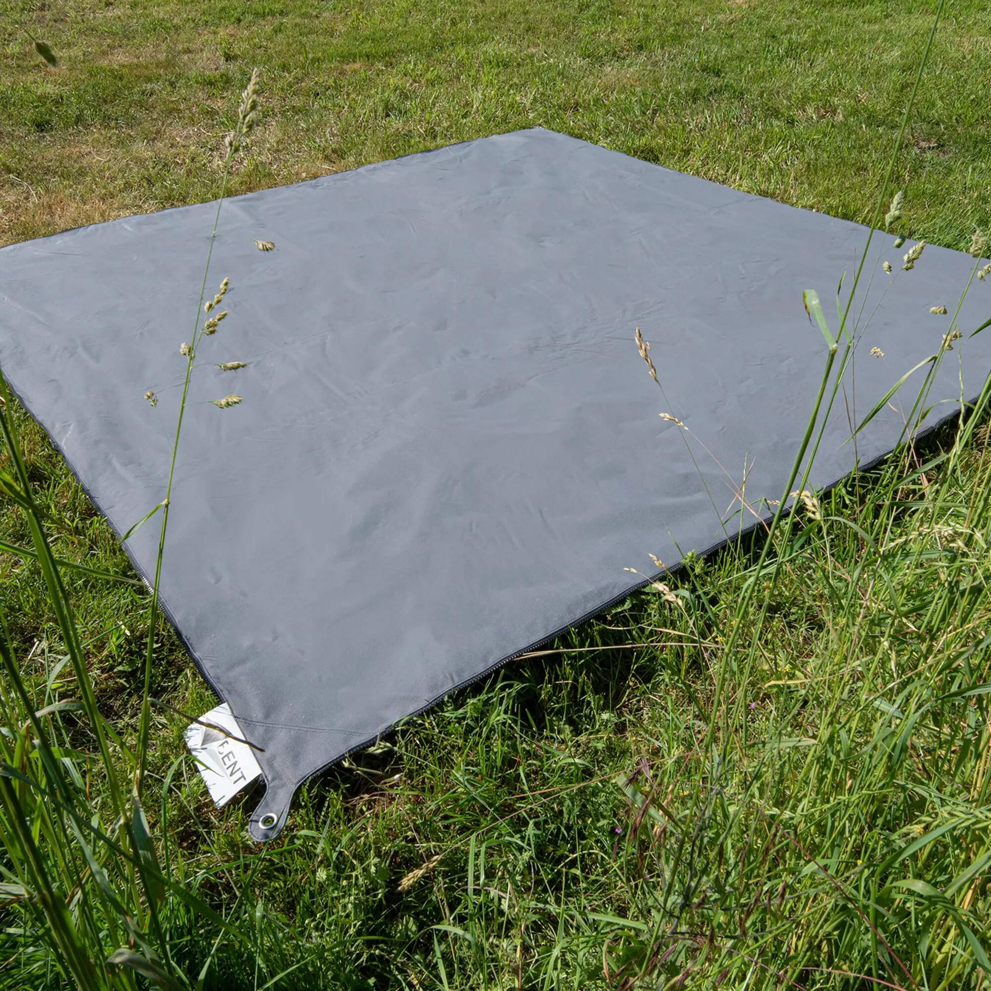 Zip Carpet in dunkelgrau liegt flach auf Gras; rechteckige Outdoor-Matte mit sichtbarer Randnaht und einem Etikett am unteren Rand