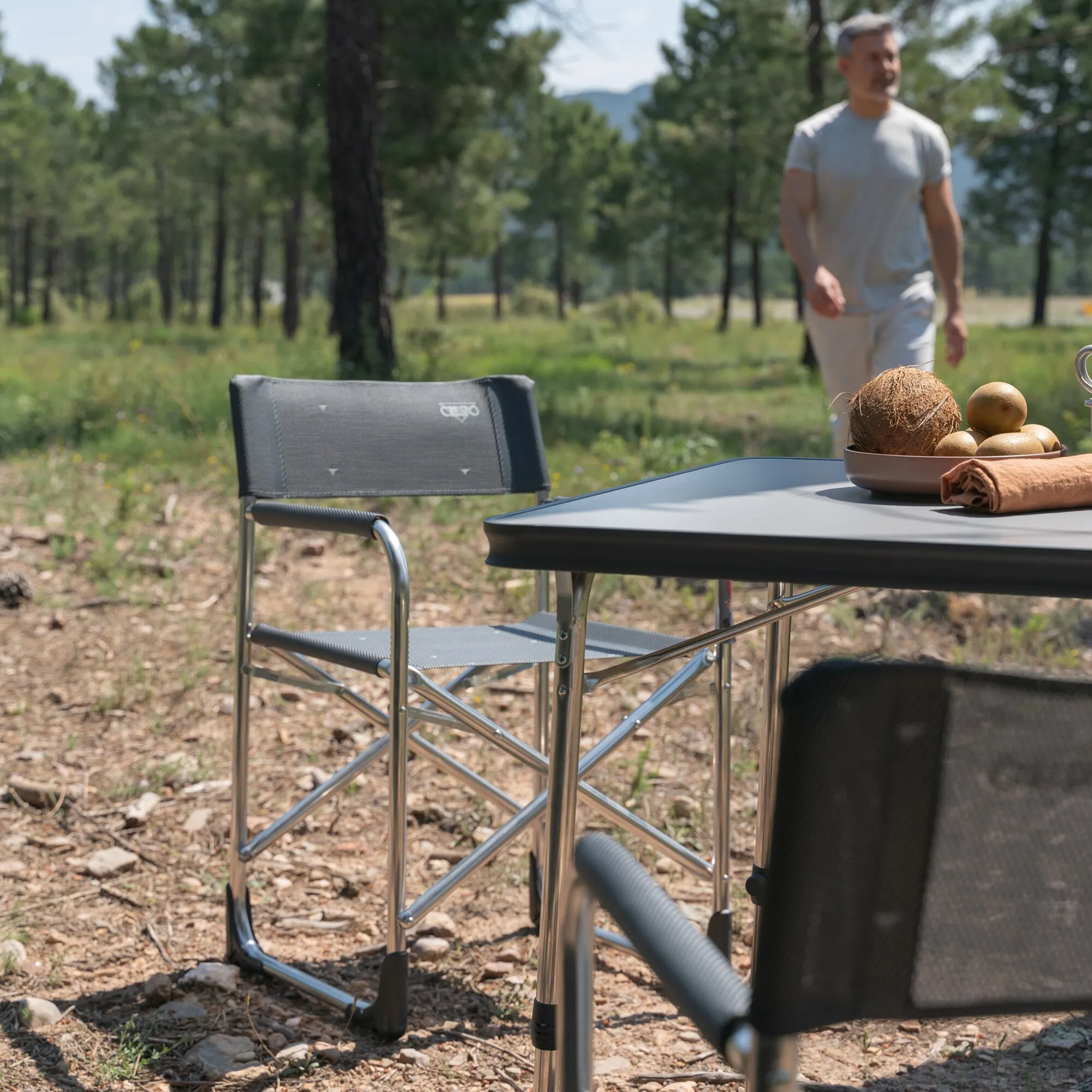 Schwarzer Regiesessel AL/214 Classic mit grauer Sitzfläche und Rückenlehne neben einem Tisch im Waldsetting