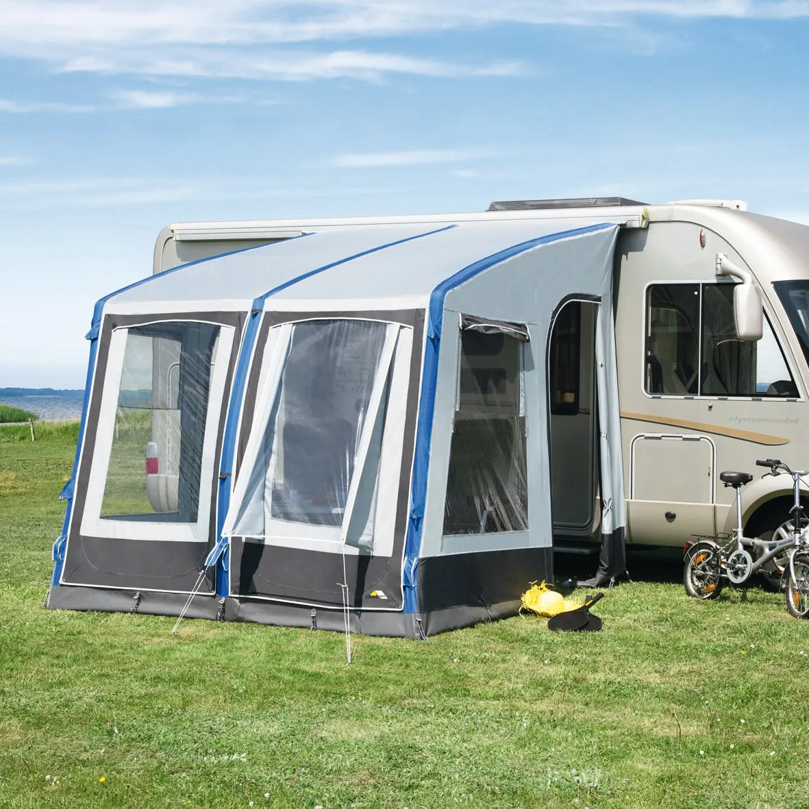 Graublaues Teilzelt Space Air HQ mit zwei großen Fenstern an einem weißen Wohnmobil auf einer Wiese am Meer