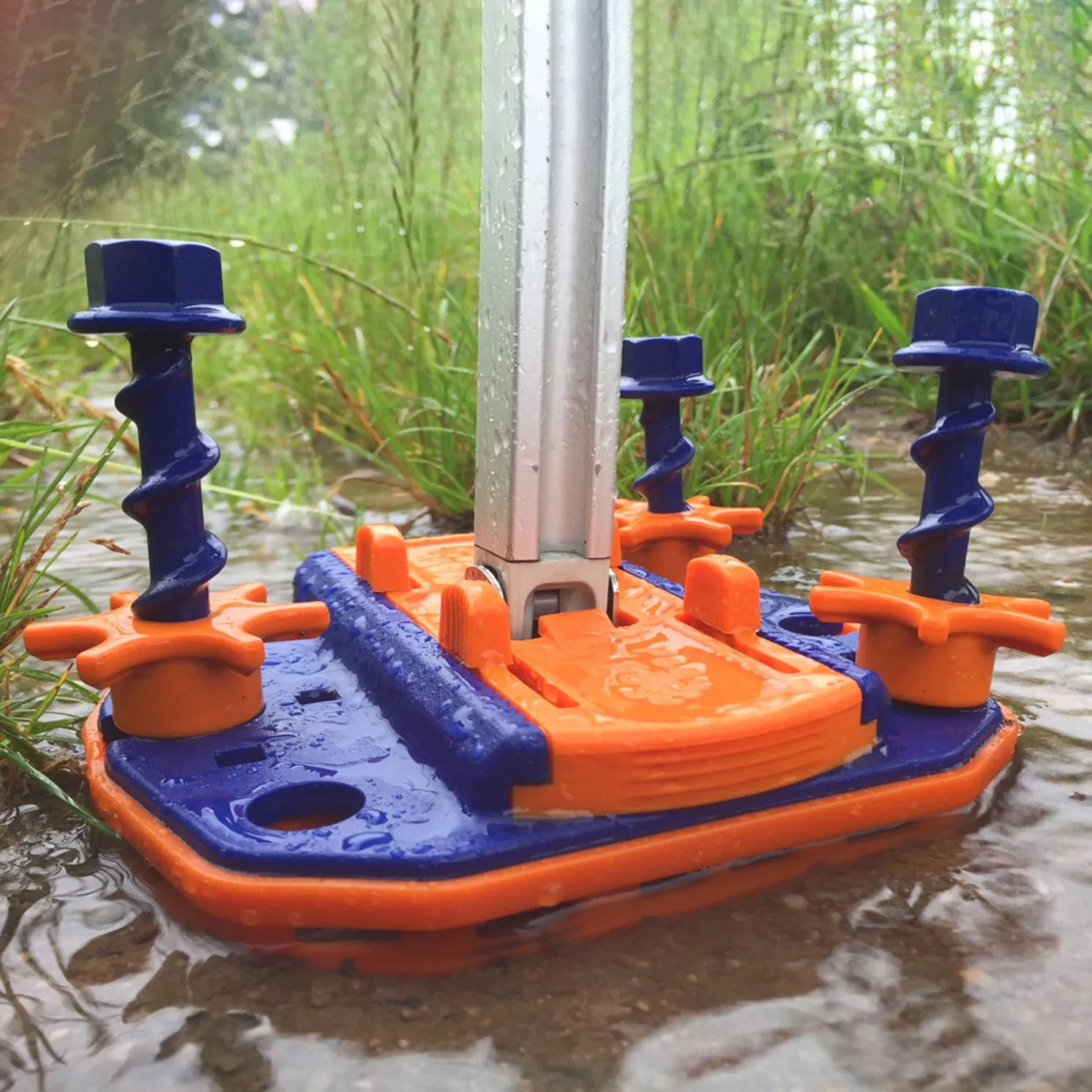 Orange-blaue PP-Abstandsplatte Fix&Go Bridge mit Befestigungselementen und Metallprofil im flachen Wasser eines Bachs