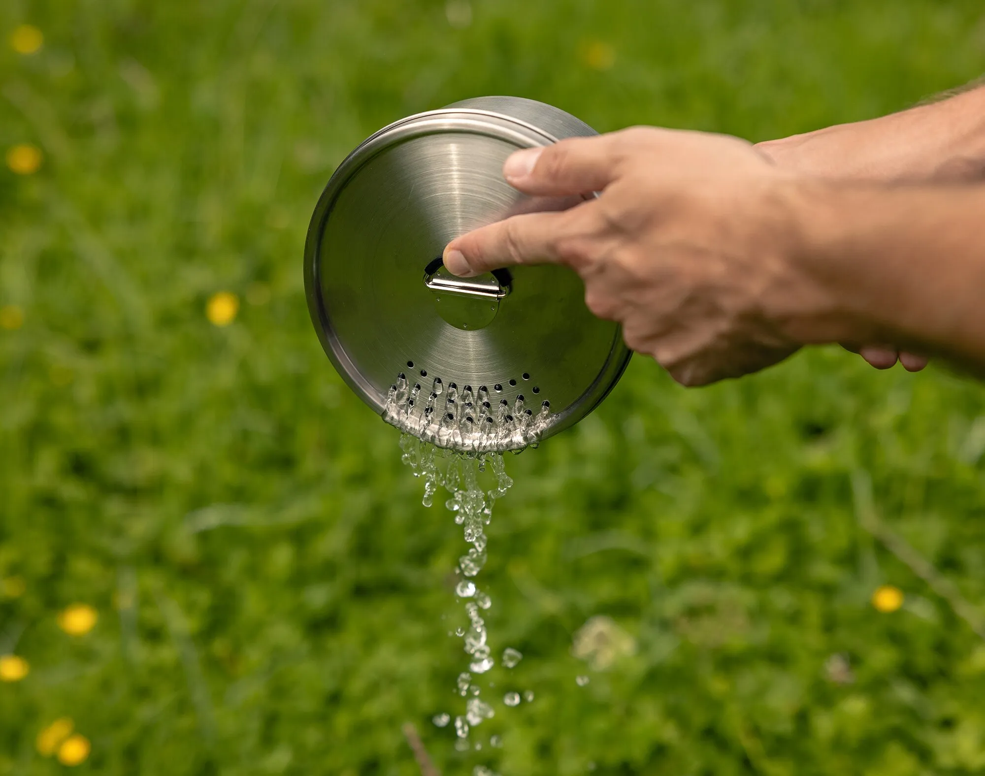Edelstahldeckel eines Trekking-Kochgeschirrsets mit Griff und Sieböffnungen, aus dem Wasser abläuft