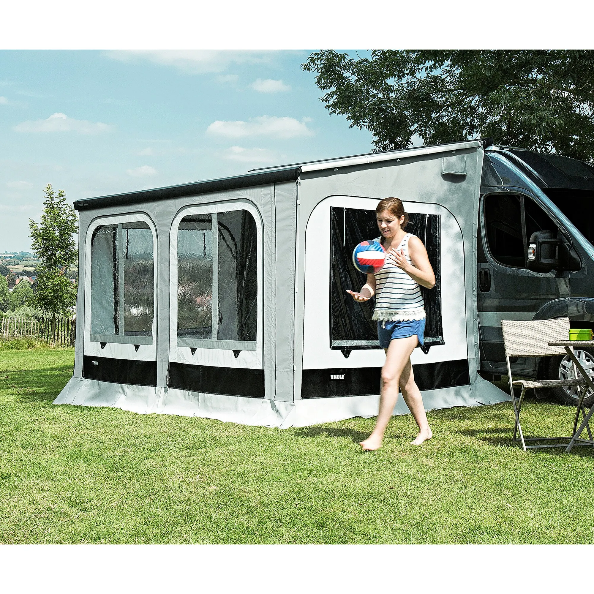 Graues Thule Panorama Ducato Markisenzelt mit Fensterfront am schwarzen Campingbus, eine Frau trägt einen Ball heraus