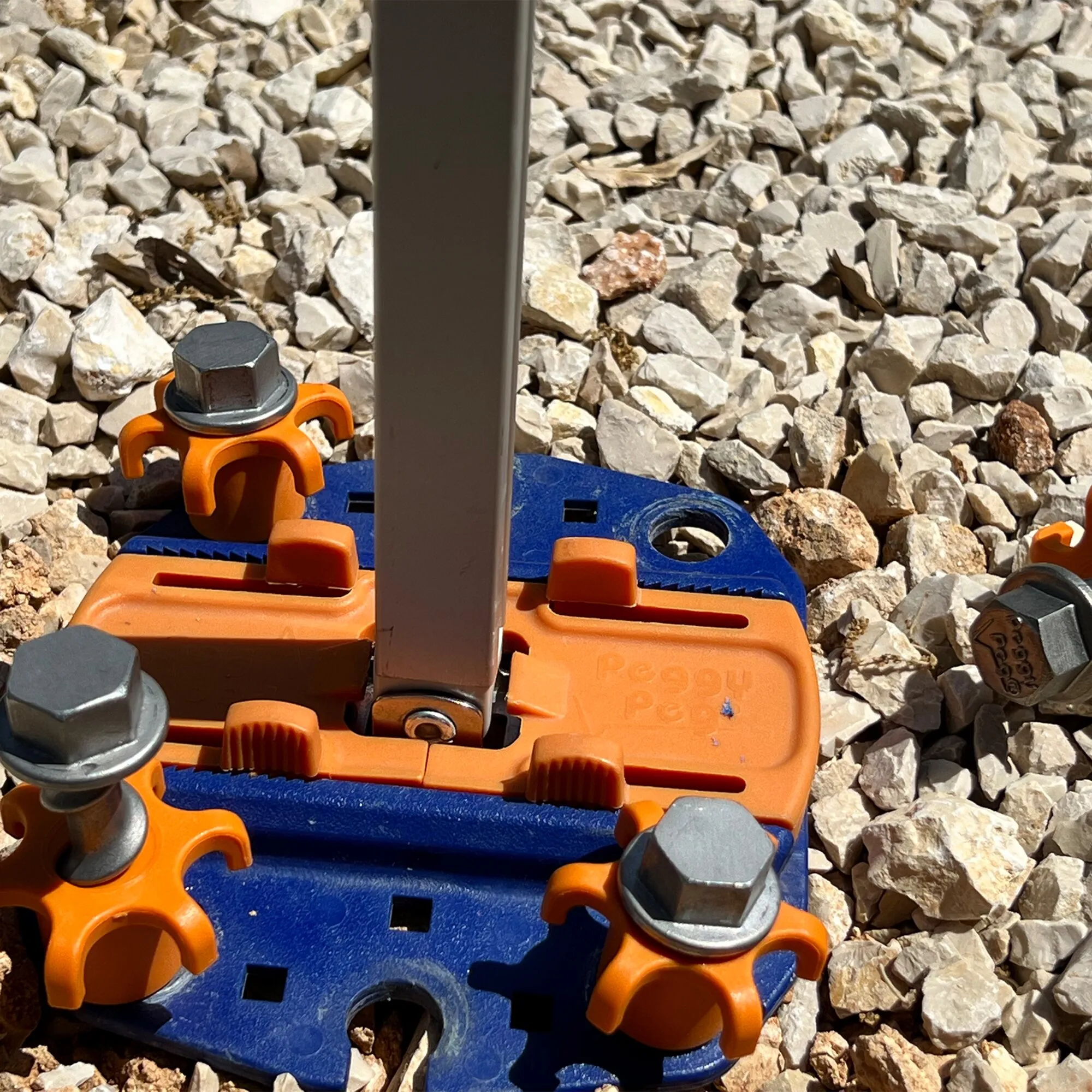 Orange-blaue Schraubheringe Peg&Stop HeavyDuty mit Sechskantköpfen, die ein vertikales Profil auf Schotter befestigen