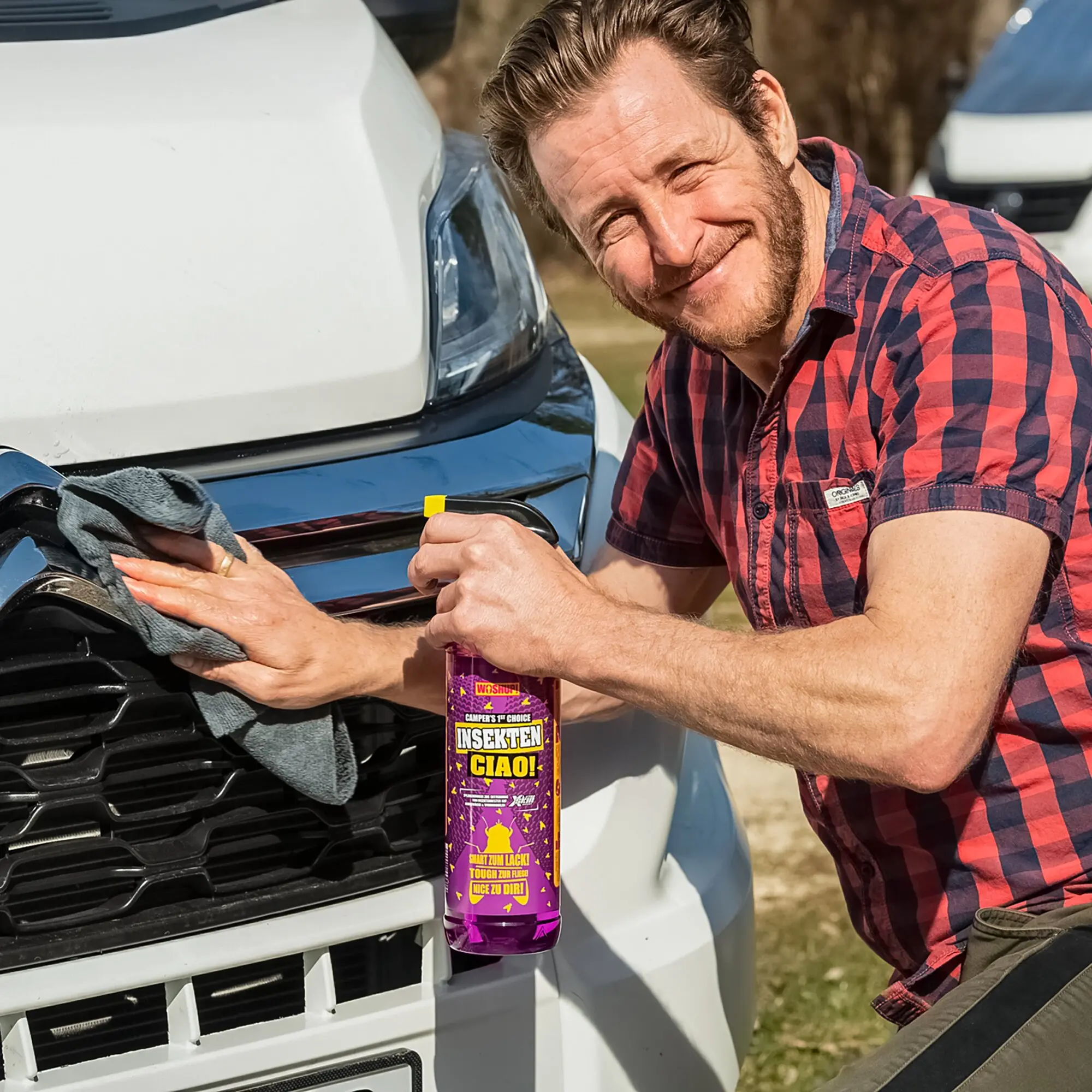 Mann in rotem Karohemd reinigt die Front eines weißen Autos; eine violette Flasche Insektenentferner CIAO wird an der Stoßstange gehalten