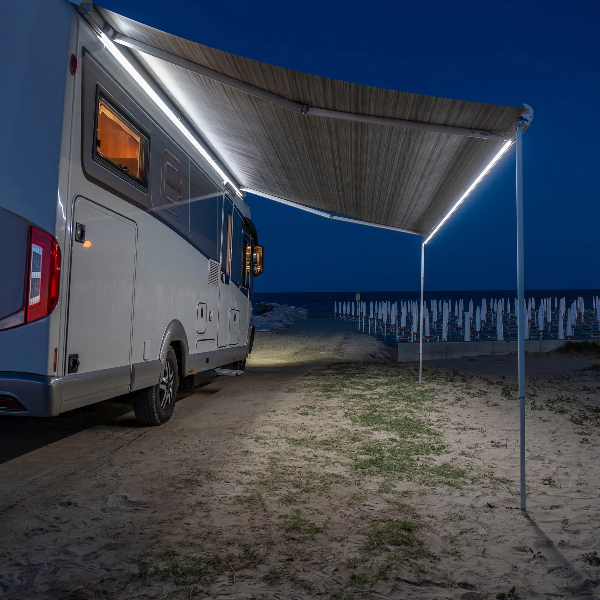 Wohnmobil mit ausgefahrener Markise und umlaufender LED-Beleuchtung des Markisenbeleuchtung Kits Strip Awning F80 am Strand bei Nacht
