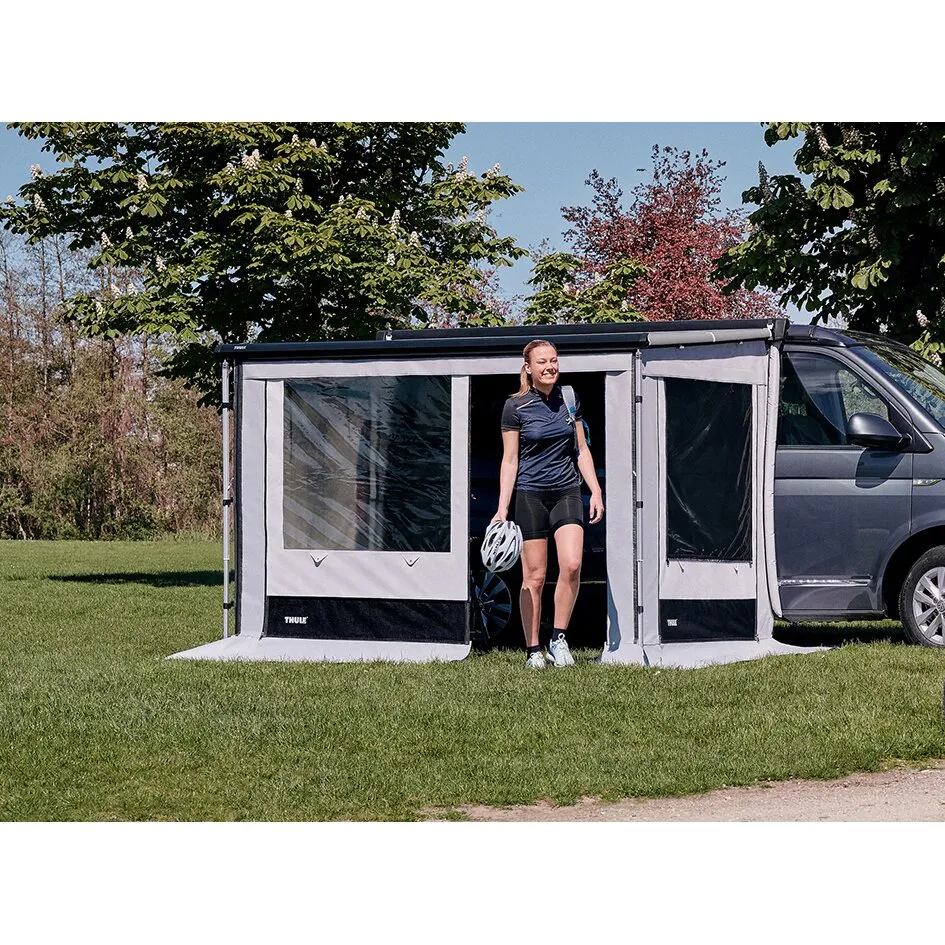 Graues Thule Residence G3 T5/T6 Vorzelt an einem Van mit geöffneter Tür, eine Frau tritt mit Fahrradhelm ins Freie