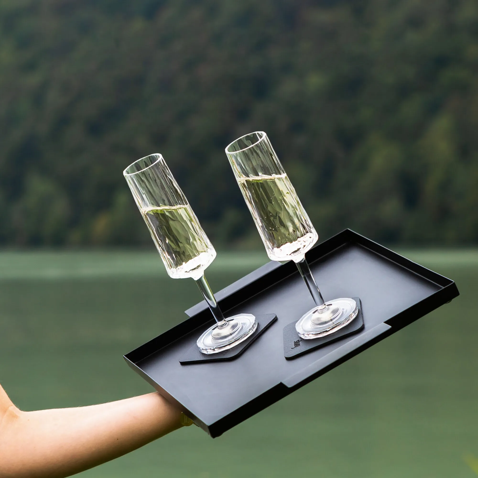 Zwei transparente Kunststoff-Sektgläser mit Reliefstruktur und gefülltem Sekt stehen auf einer schwarzen Magnetplatte in einem Tablett