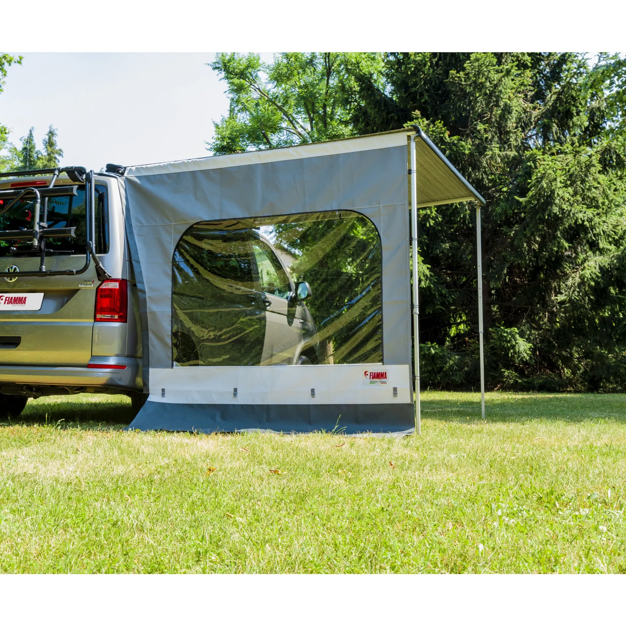 Graue Fiamma-Seitenwand Side W Pro F40 an einem Wohnmobil mit großem transparentem Fenster und Markisenstützen im Grünen